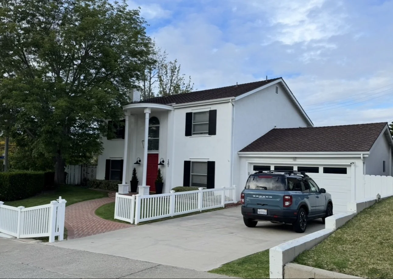 Two-story colonial home exterior — white siding, black shutters, red entry door with picket fence