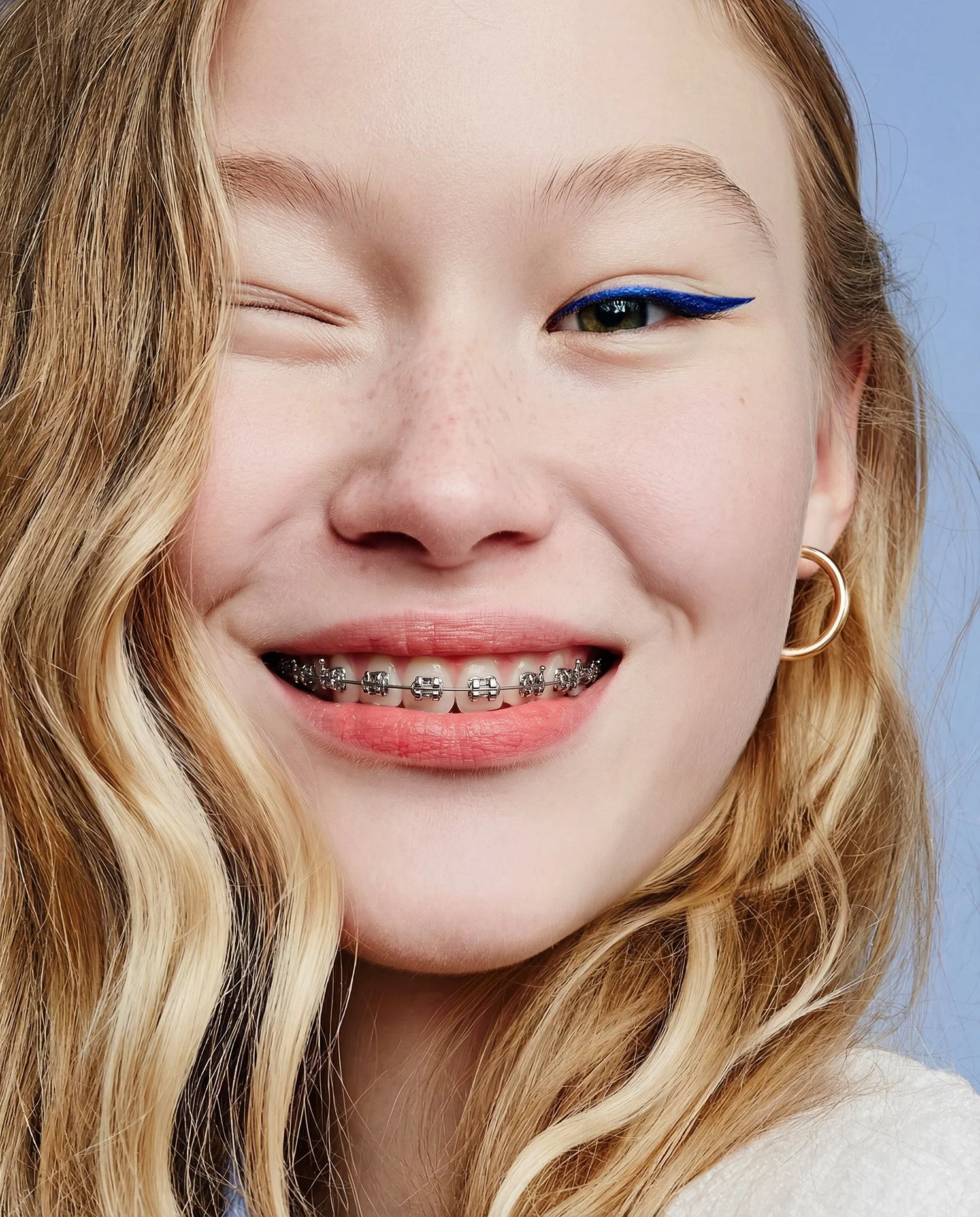 Close portrait of a teenage girl laughing, braces and blue liner. AI-generated image.