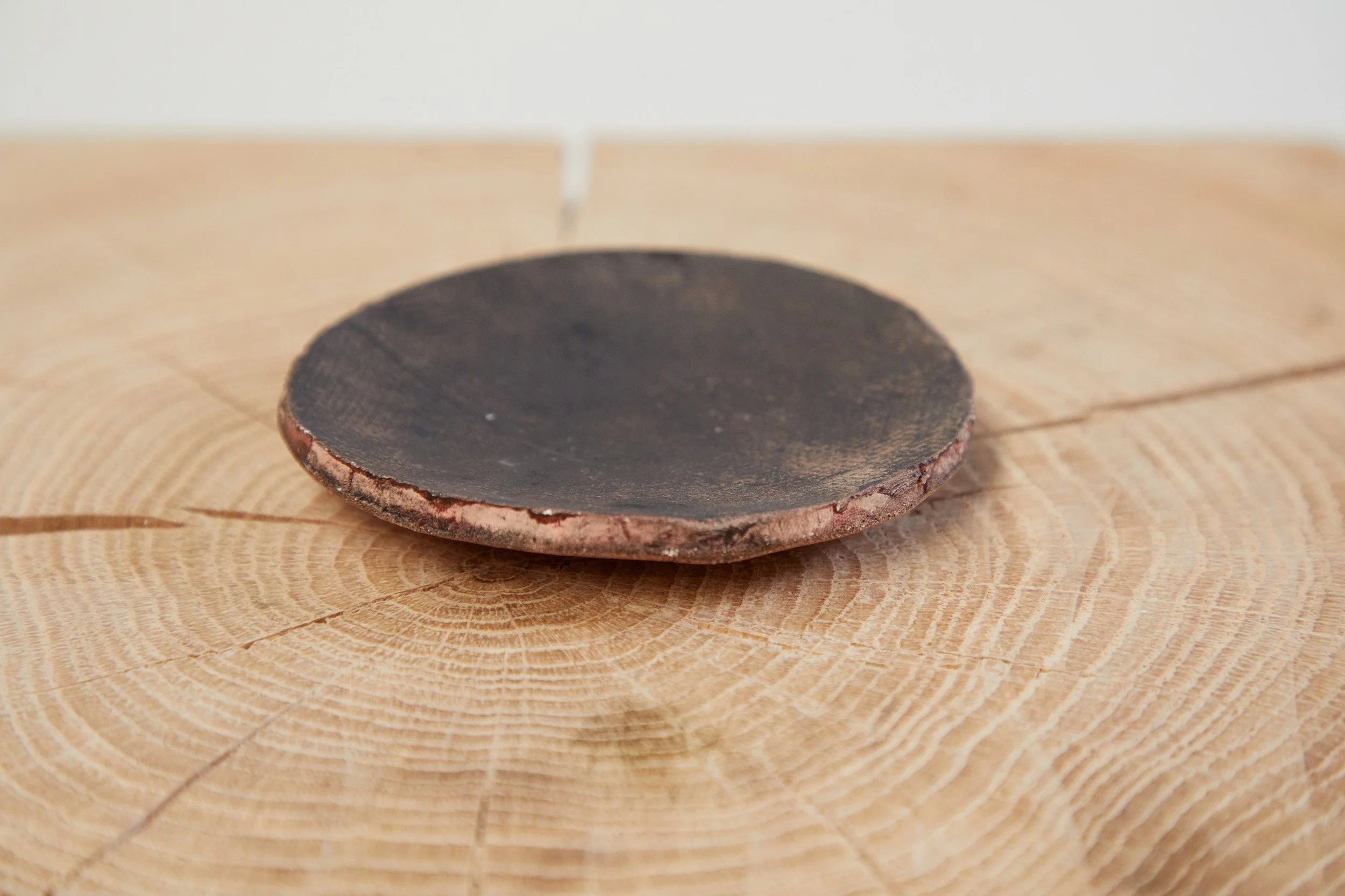 Dark brown hand-made ceramic plate on a tree trunk slice.