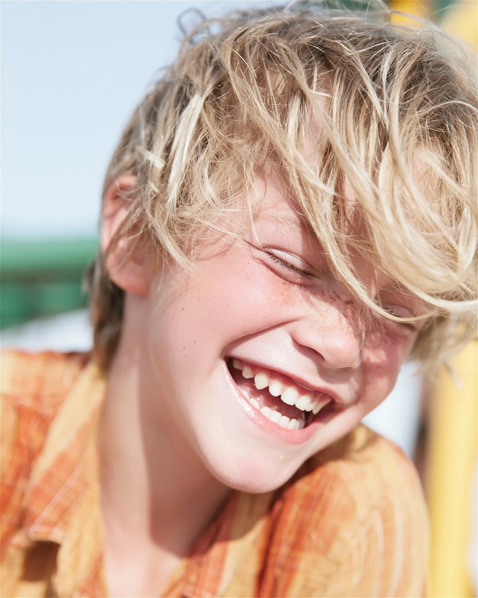 Boy laughing with his hair across his face, orange shirt. AI-generated image.