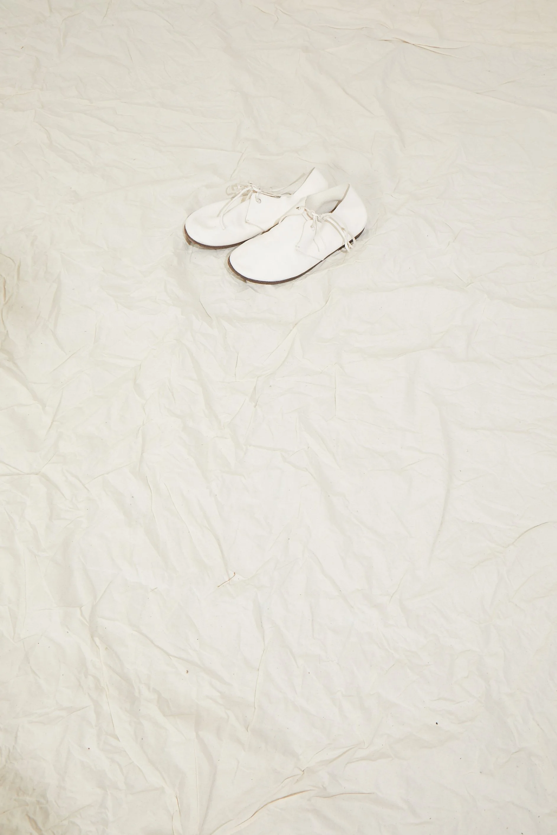 White leather shoes on crumpled ecru fabric