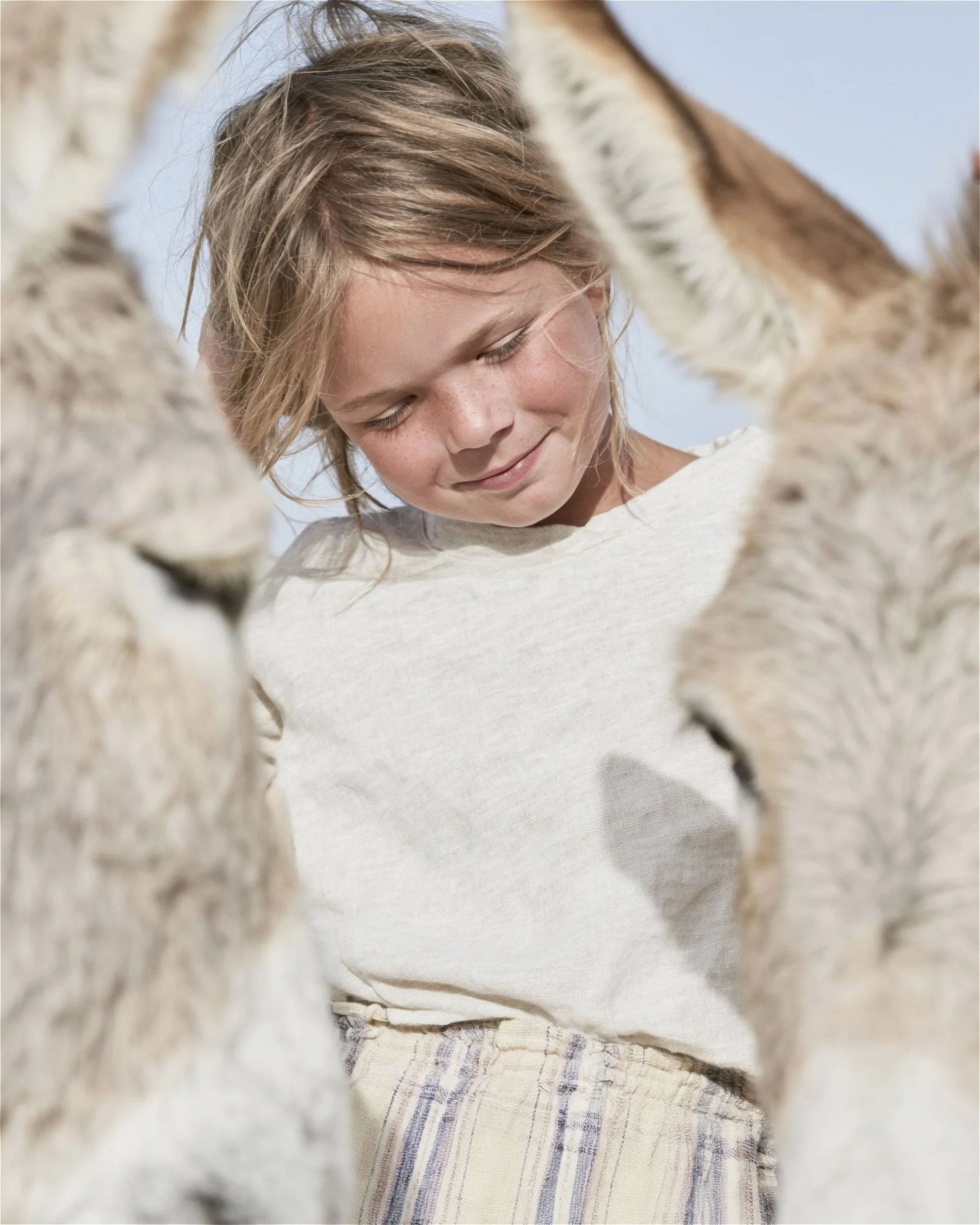 Girl in a linen top standing among donkeys. AI-generated image