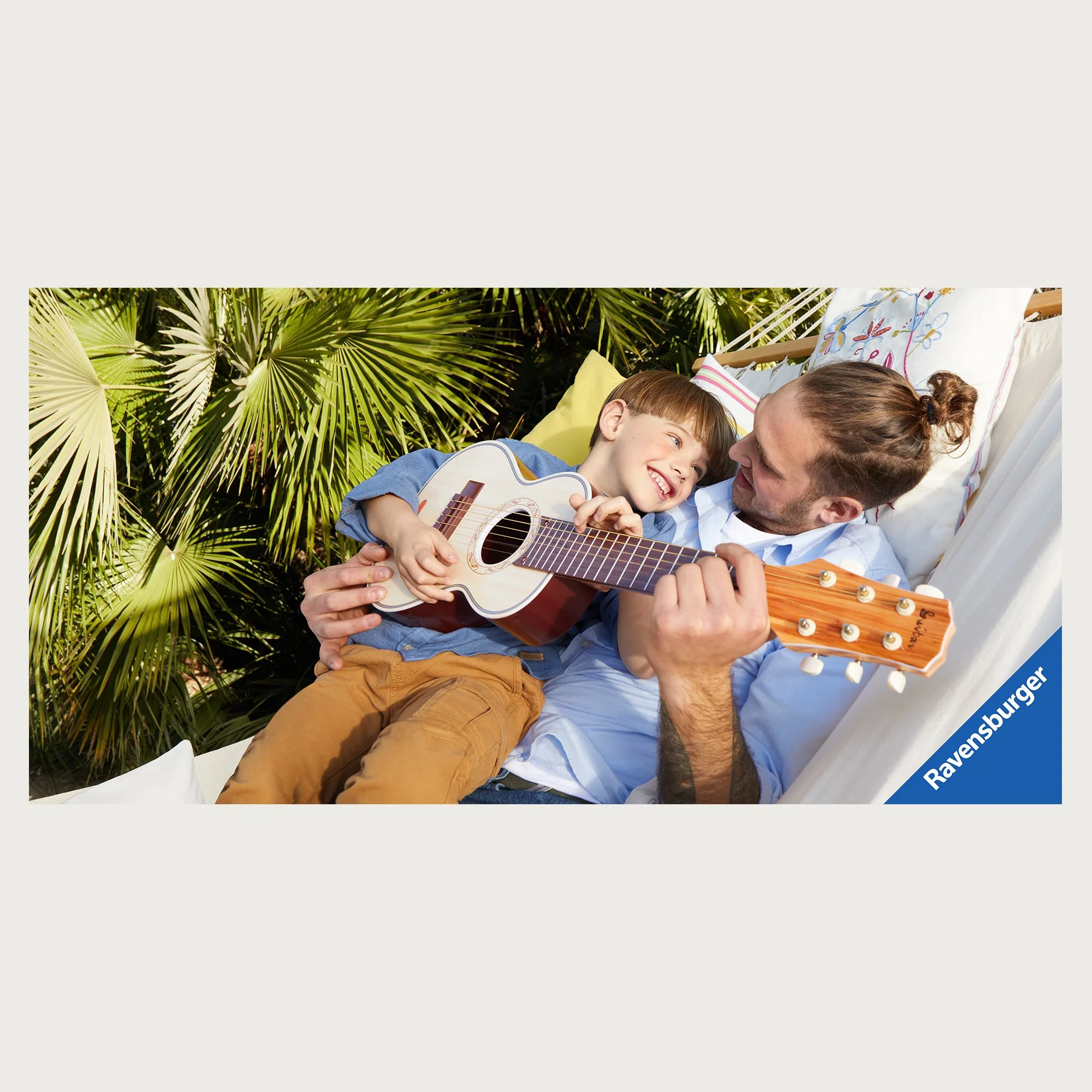Wooden toy guitar played by father and son in a hammock among palms. Ravensburger catalogue.