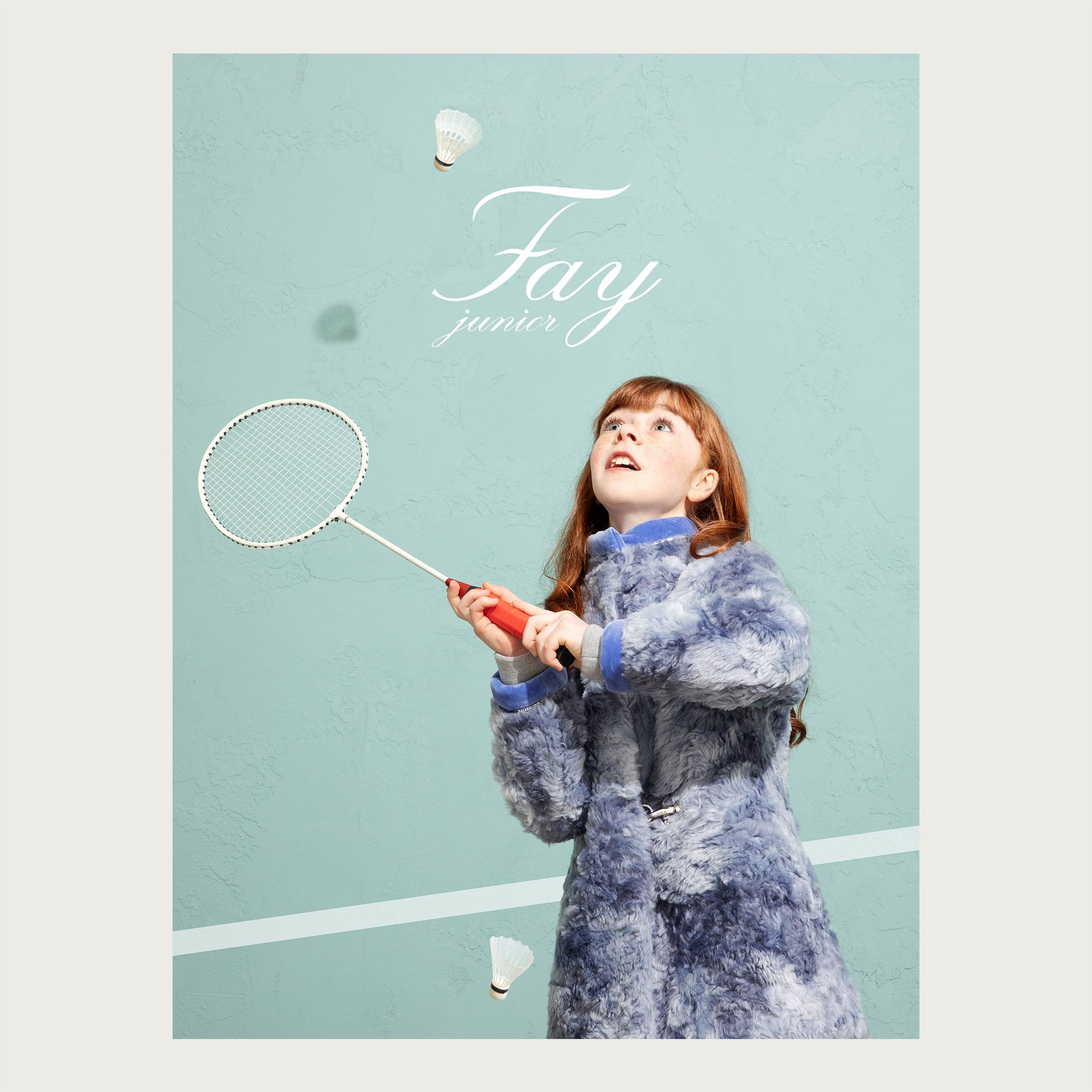 Blue-grey coat, girl serving a shuttlecock on a mint green court — Fay Junior campaign.