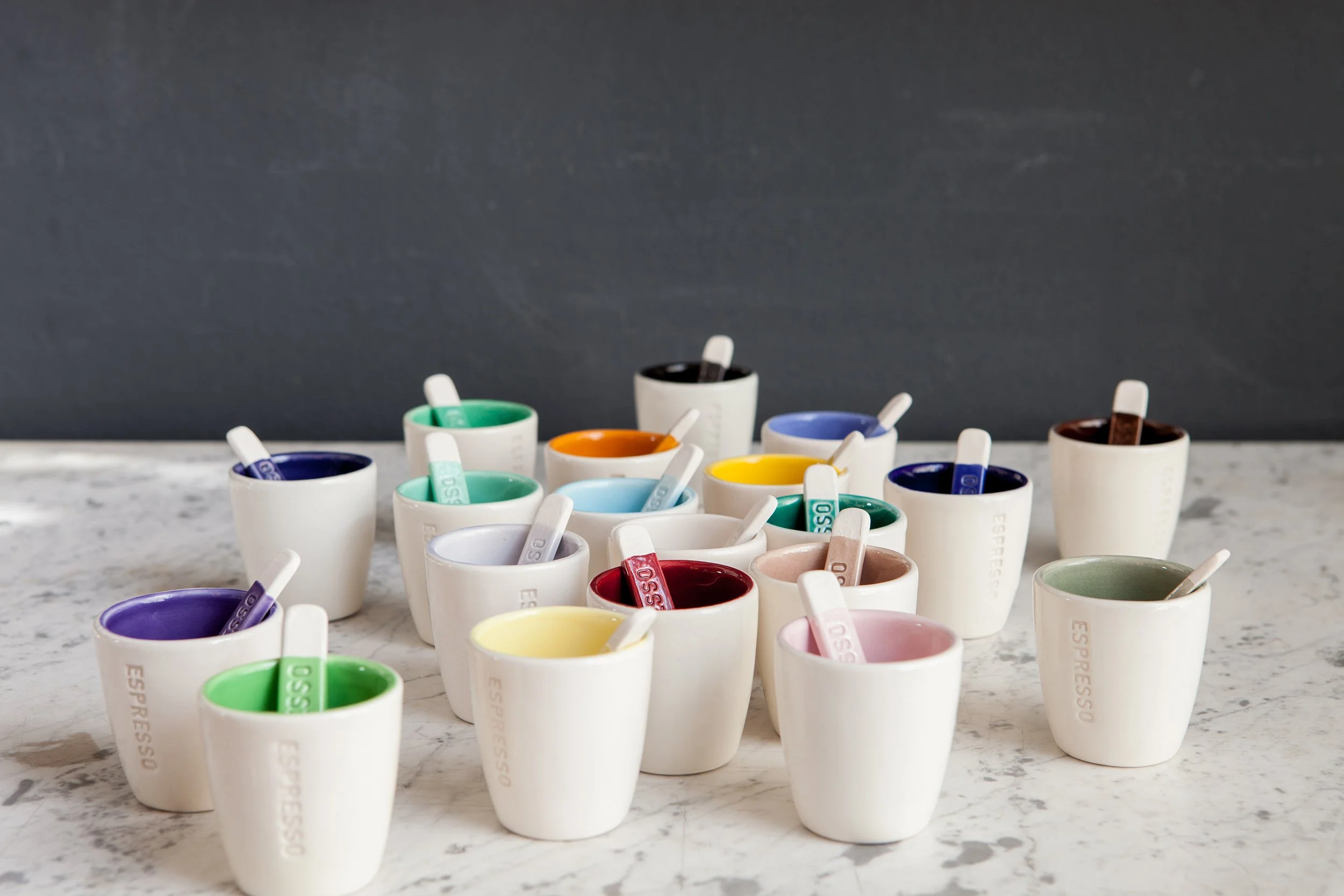 Colourful ceramic mugs with spoon on marble.