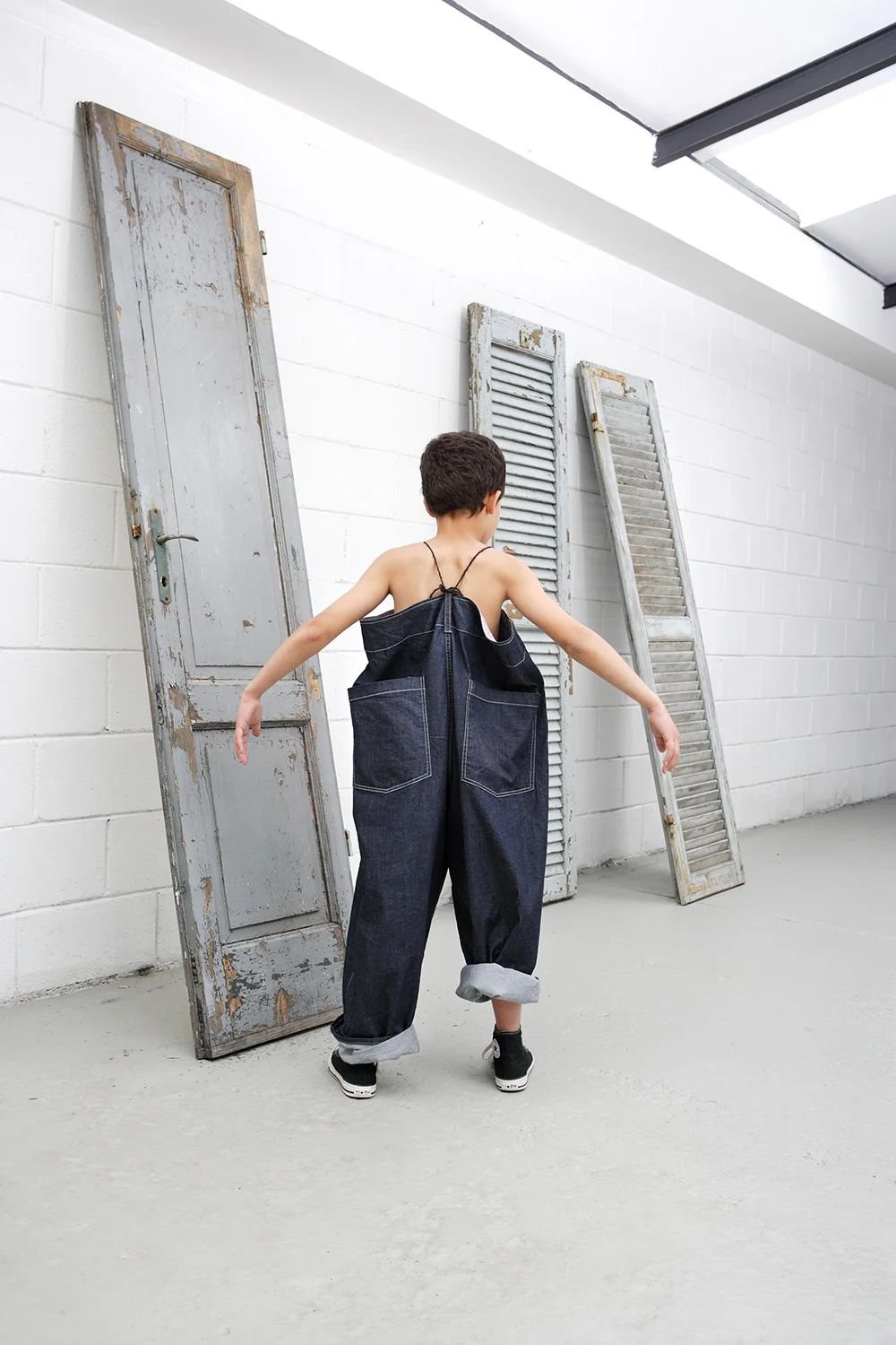 Child in denim dungarees among old wooden doors in a white location.