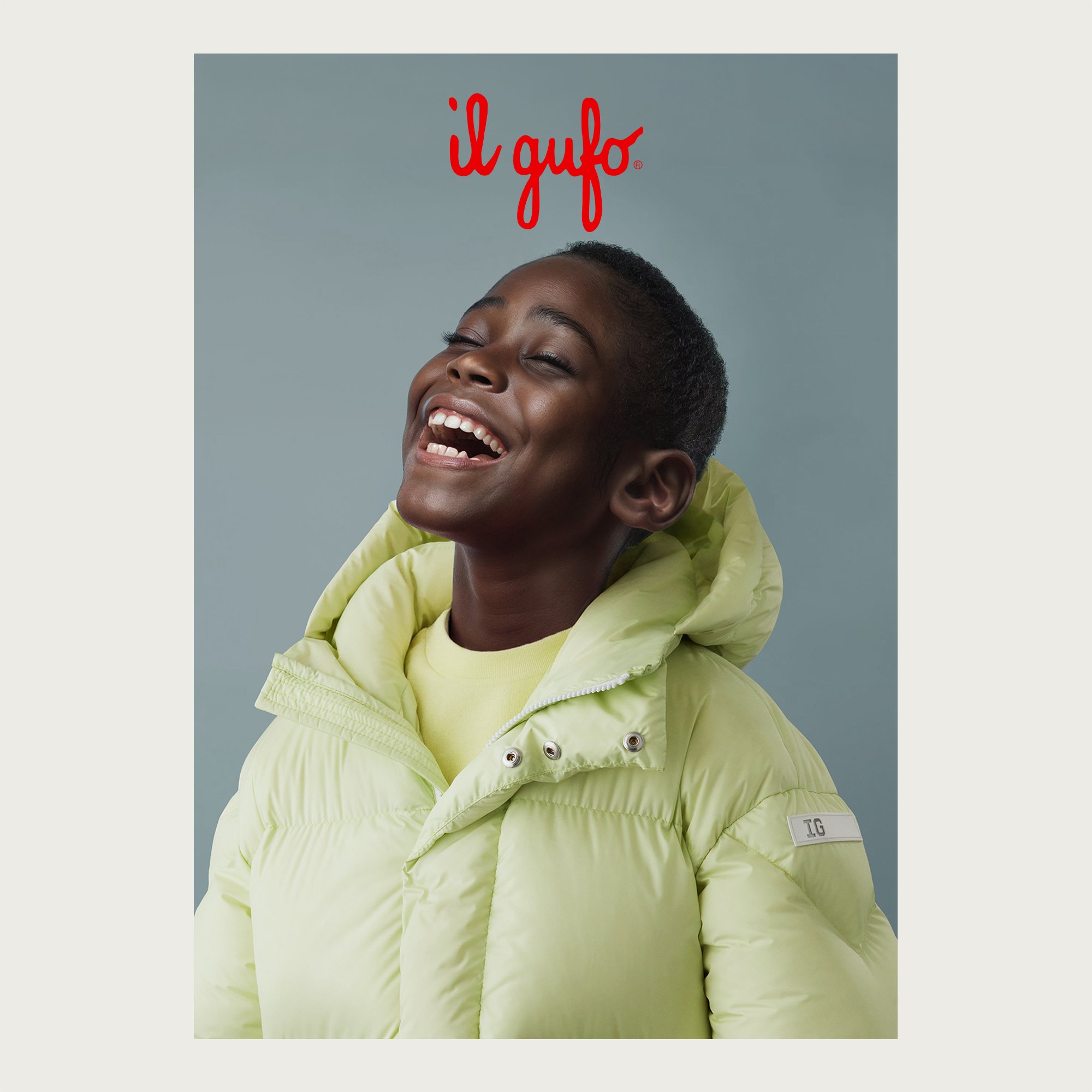 Lime green hooded puffer jacket, boy laughing head back on grey-blue — Il Gufo campaign, AI-generated image.