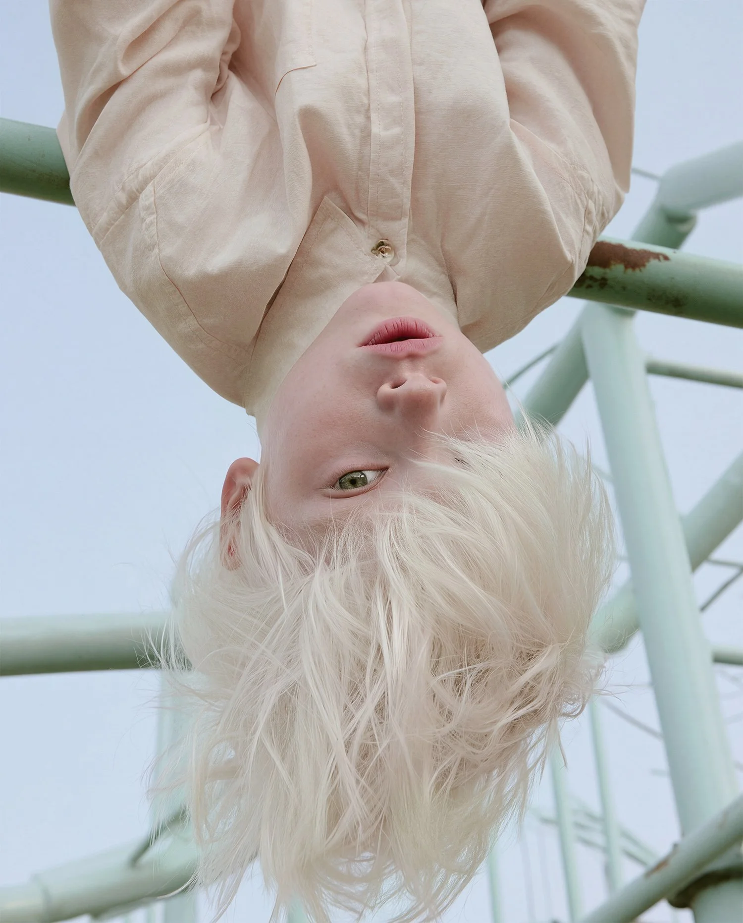 Child hanging upside down from a pale climbing frame, white hair falling. AI-generated image.