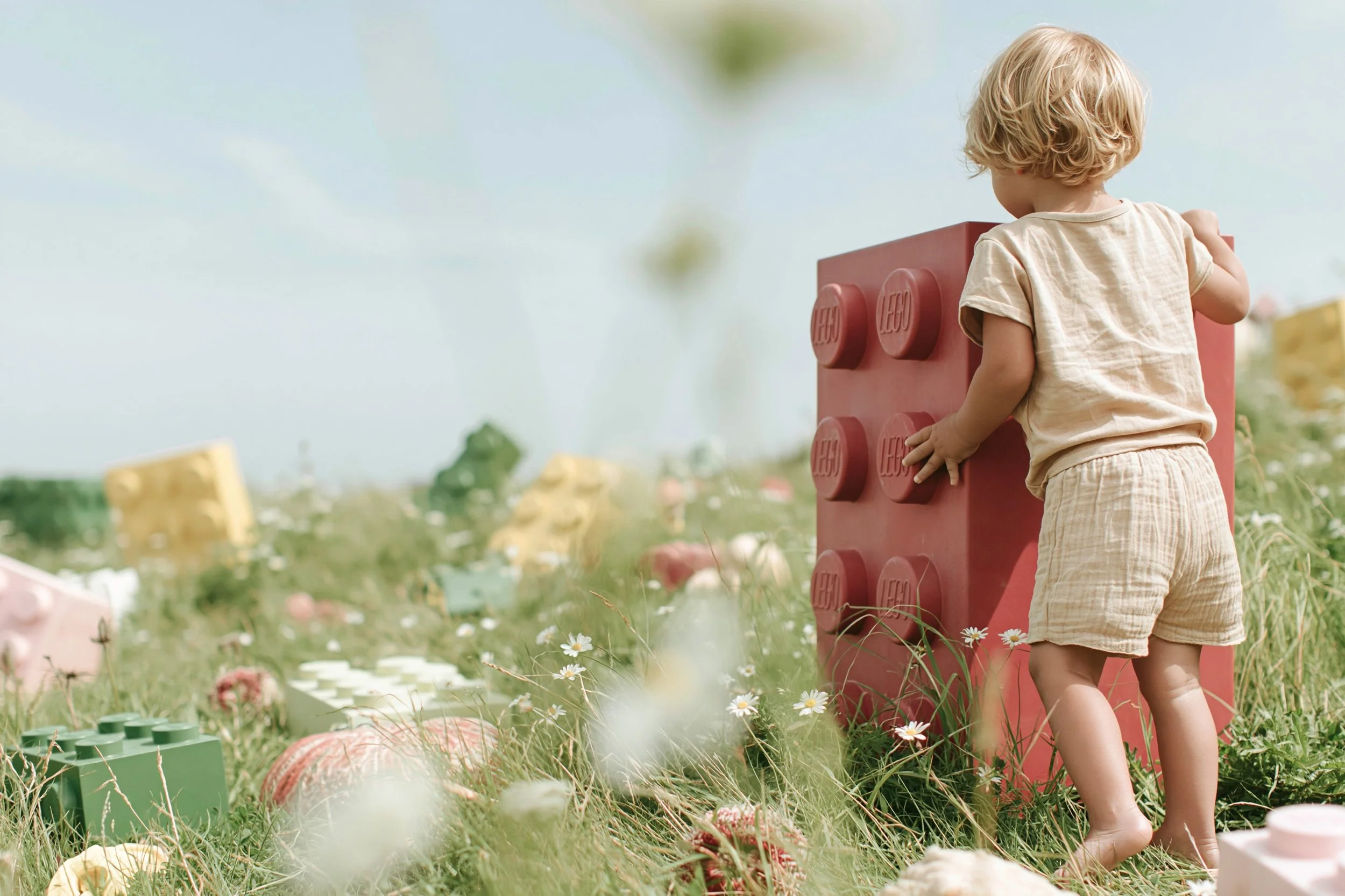 Toddler beside an oversized toy brick in a flowering meadow. AI-generated image.