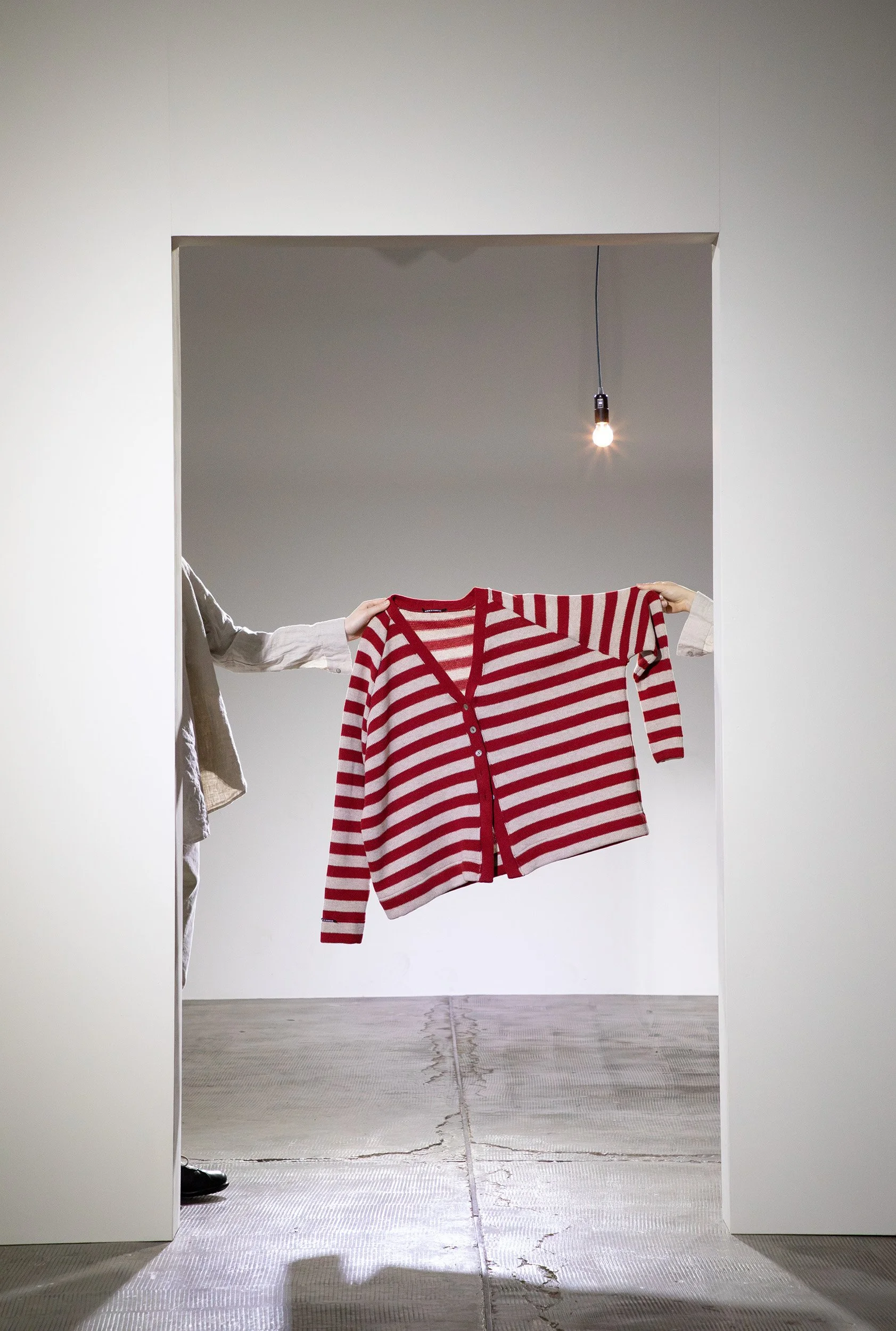 Red striped cardigan held up in a white doorway with a bare bulb.