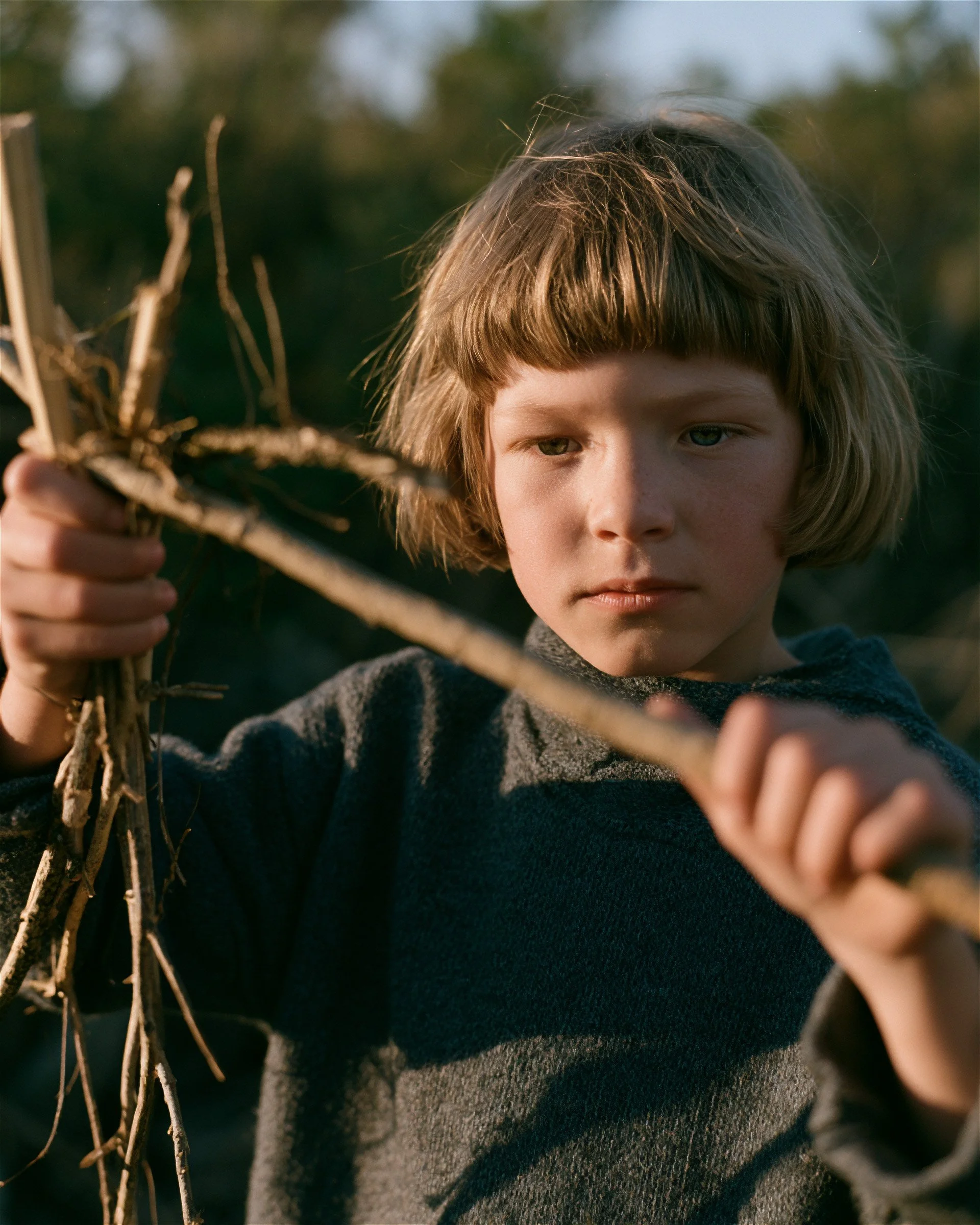 Child holding dry branches, close, afternoon light. AI-generated image.