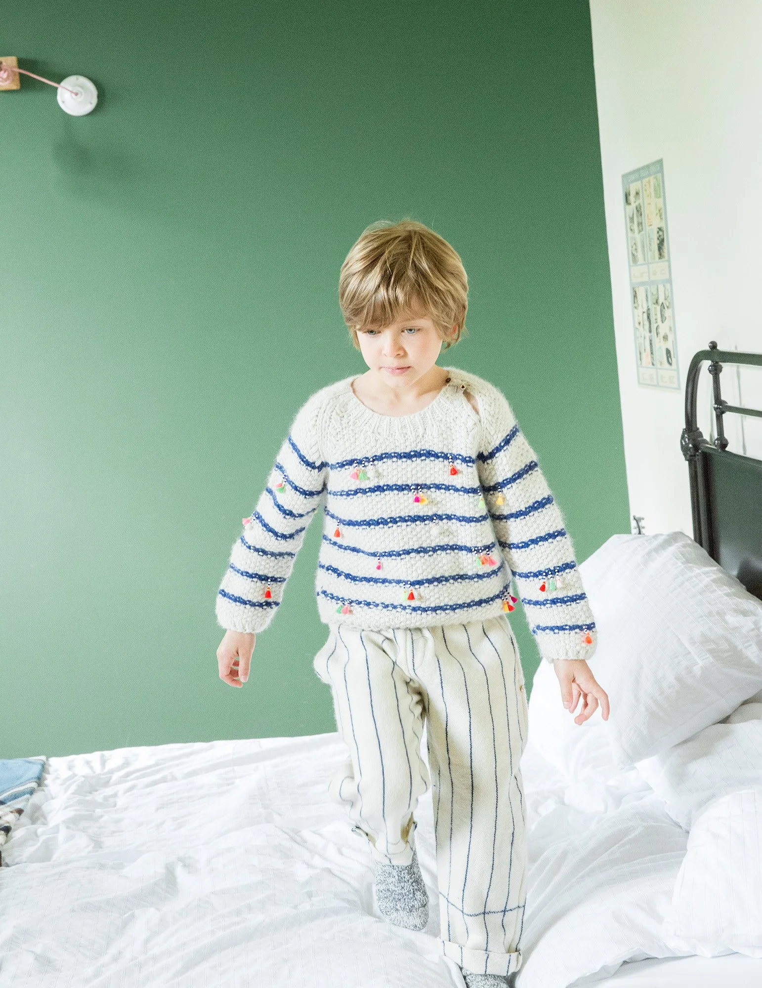 Style Piccoli editorial — boy in striped knitwear jumping on a bed against a green wall.