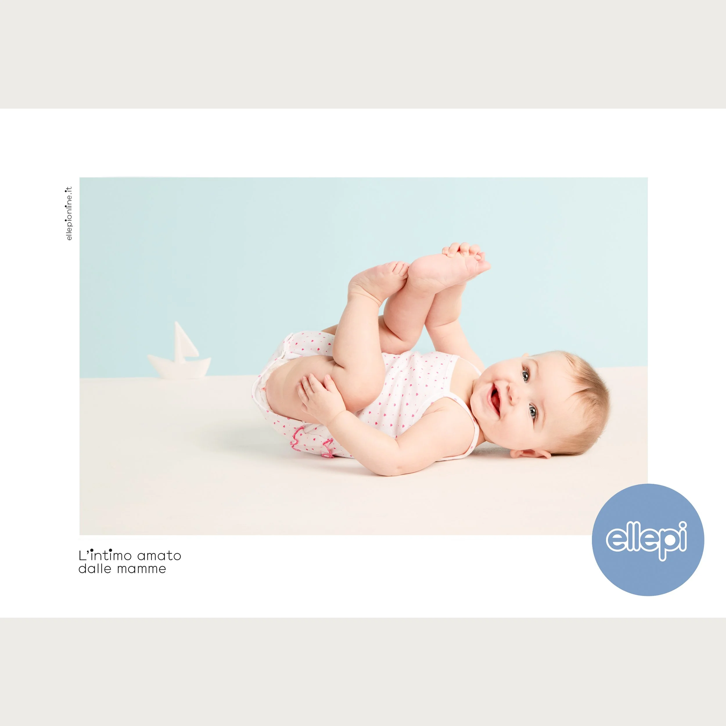 Heart-print cotton vest and bloomers, baby rolling on her side beside a paper boat — Ellepi campaign.