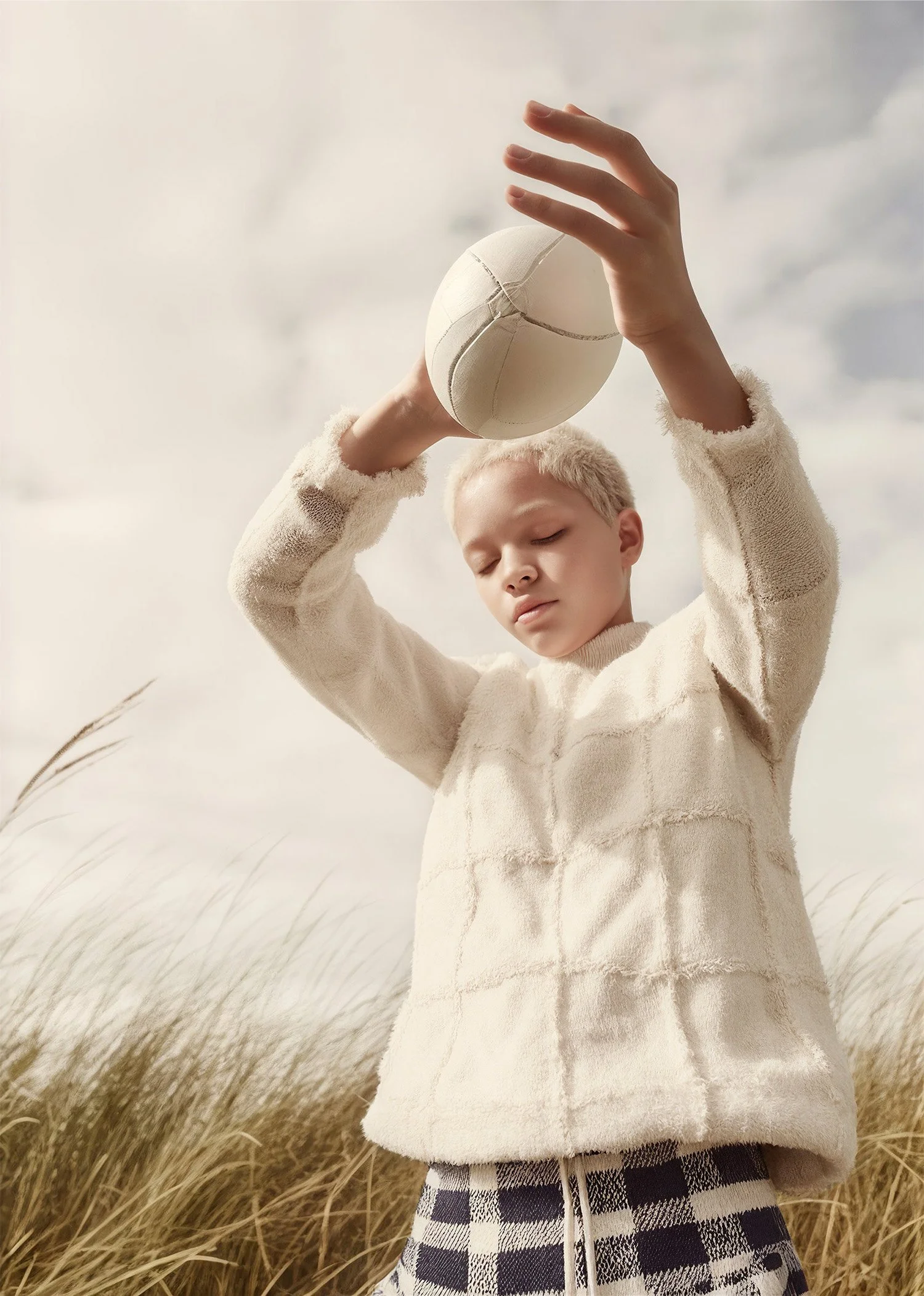 Child in a quilted jacket catching a white ball against a pale sky. AI-generated image.