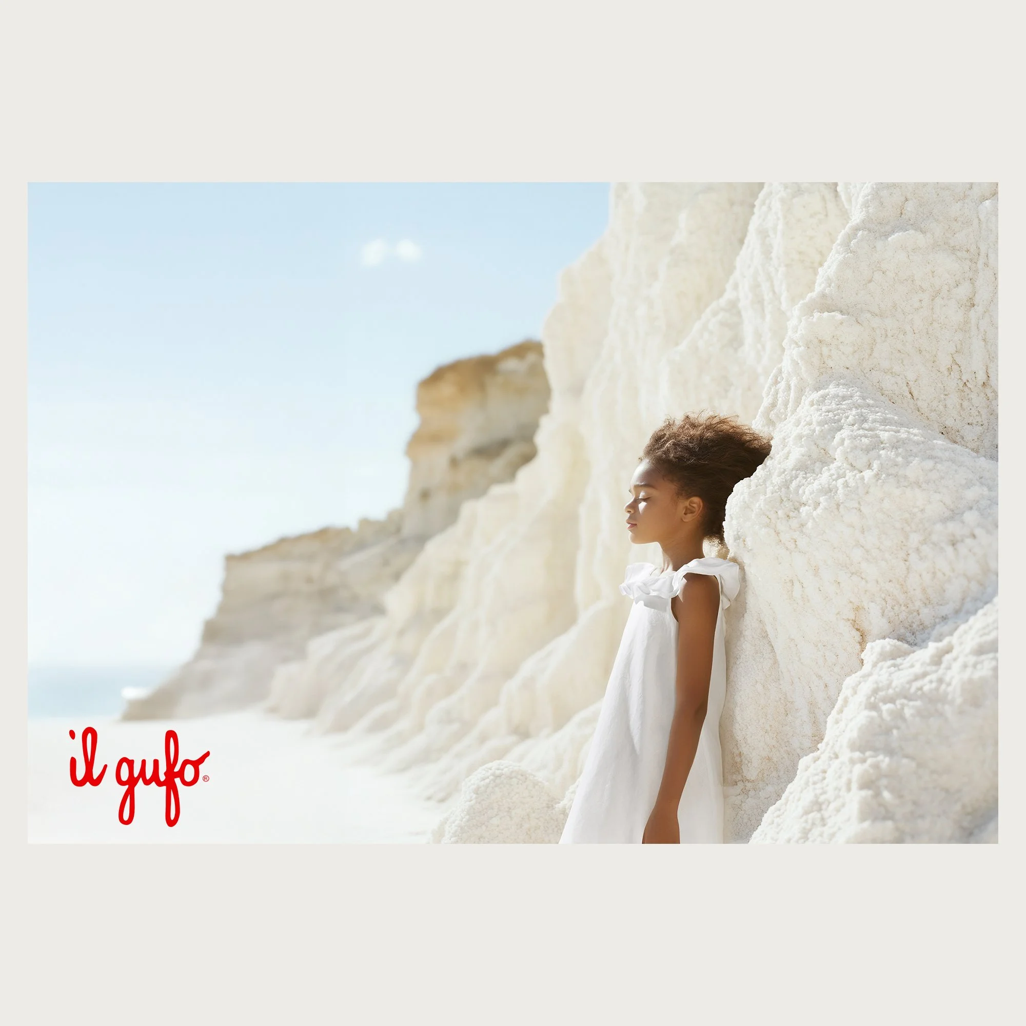 White ruffled linen dress against white salt cliffs  . Il Gufo Atelier campaign, AI-generated image.