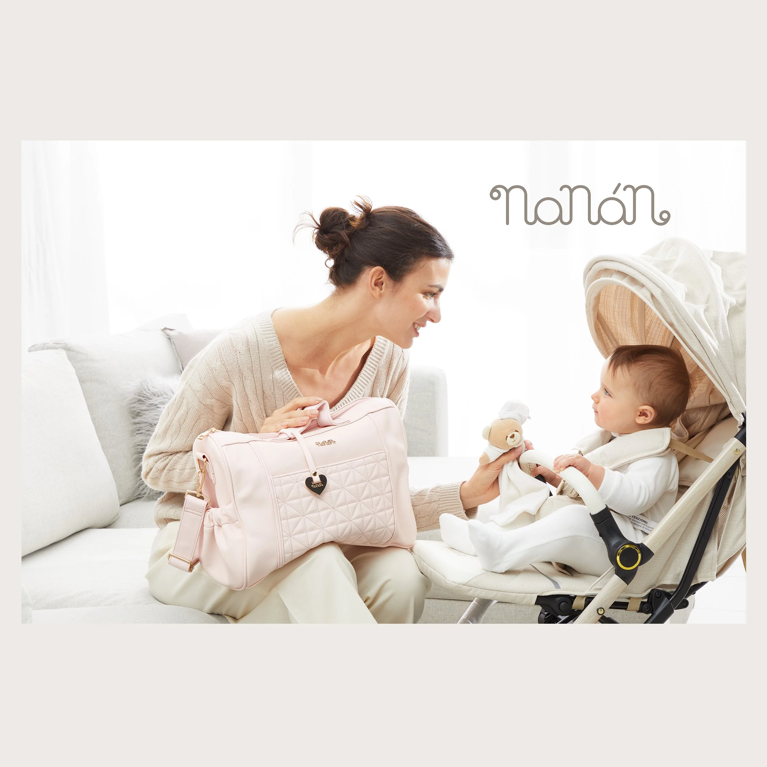 Quilted pink changing bag and knit stroller liner, mother and baby on a white sofa — Nanán campaign.