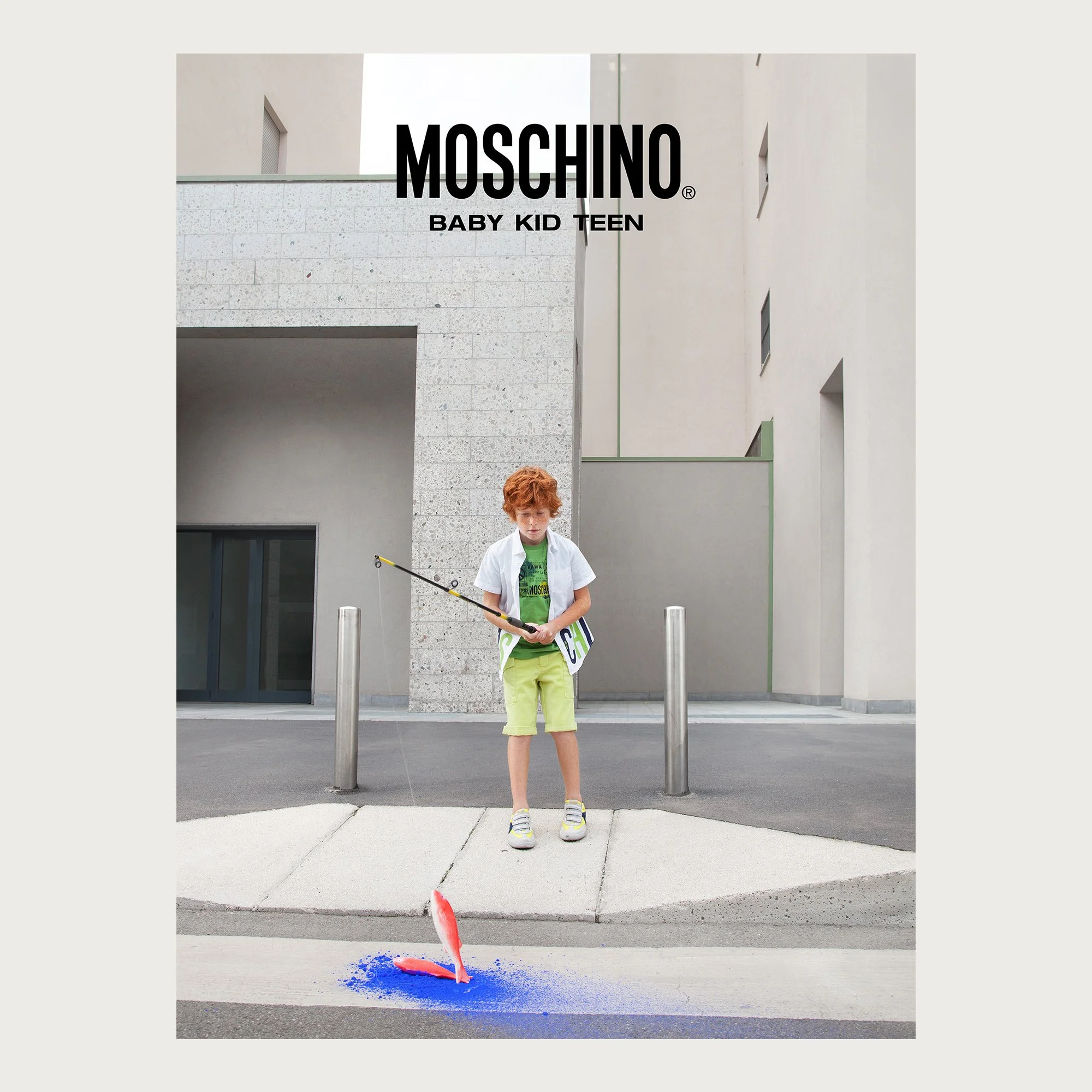 Green tee and lime shorts, boy fishing a pink fish from blue powder on a crosswalk — Moschino Kid campaign.