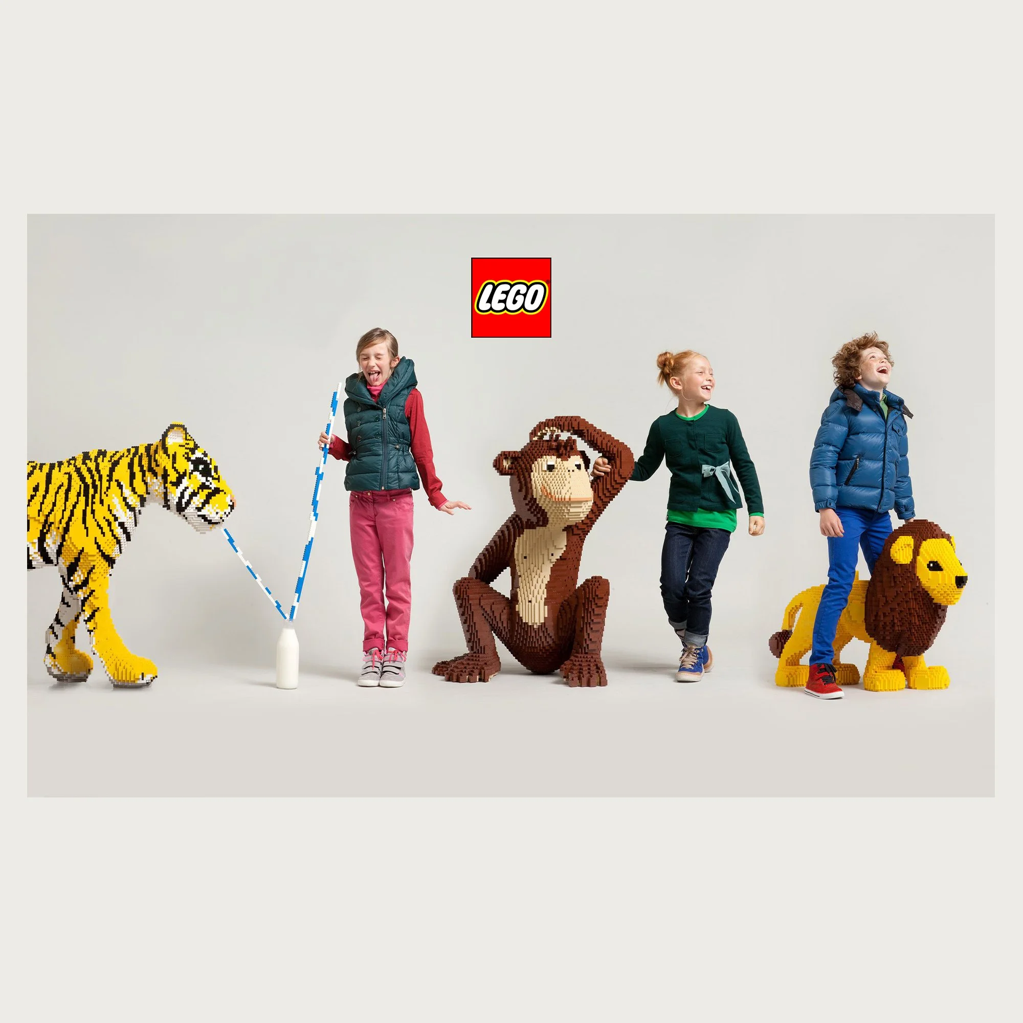 Life-size brick tiger, monkey and lion walked by three children on grey seamless. Lego editorial.