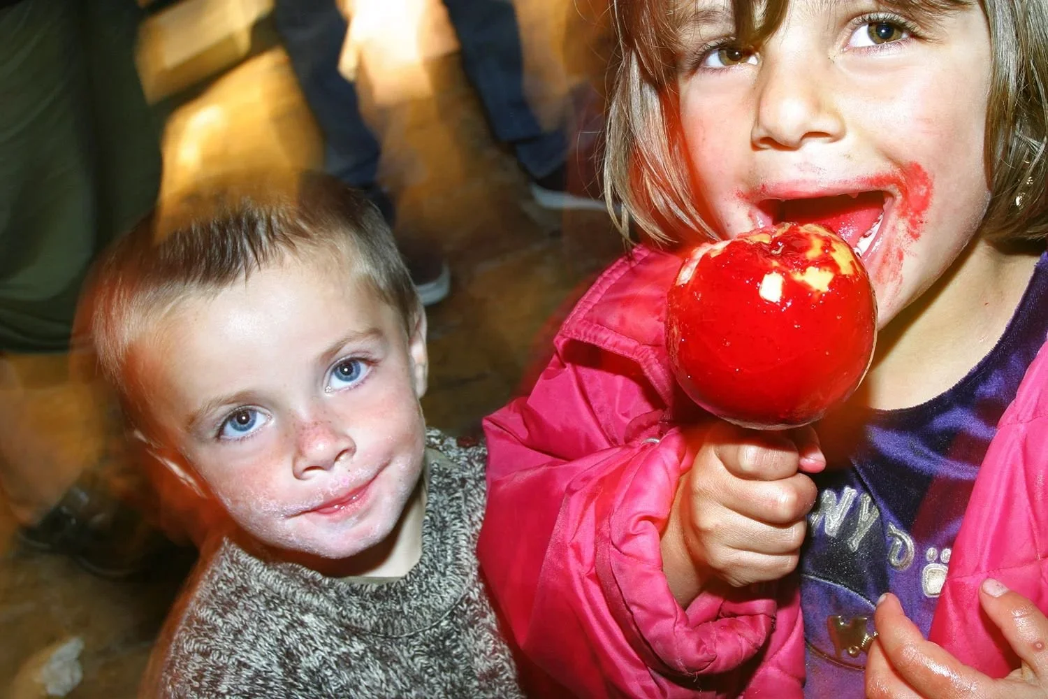 Two children at a fair, a red toffee apple caught mid-bite.