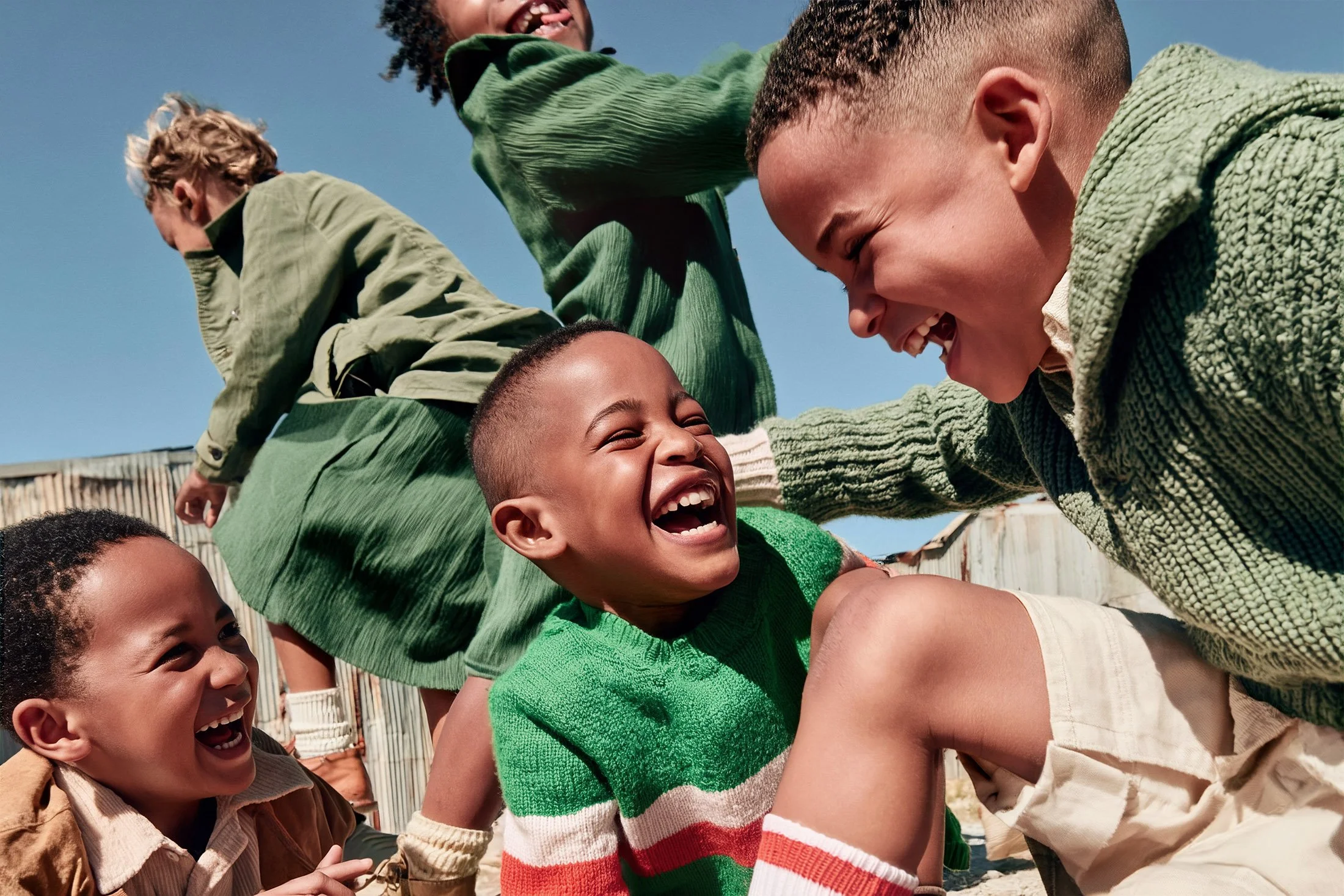 Five children in green knits laughing in a heap. AI generated image.