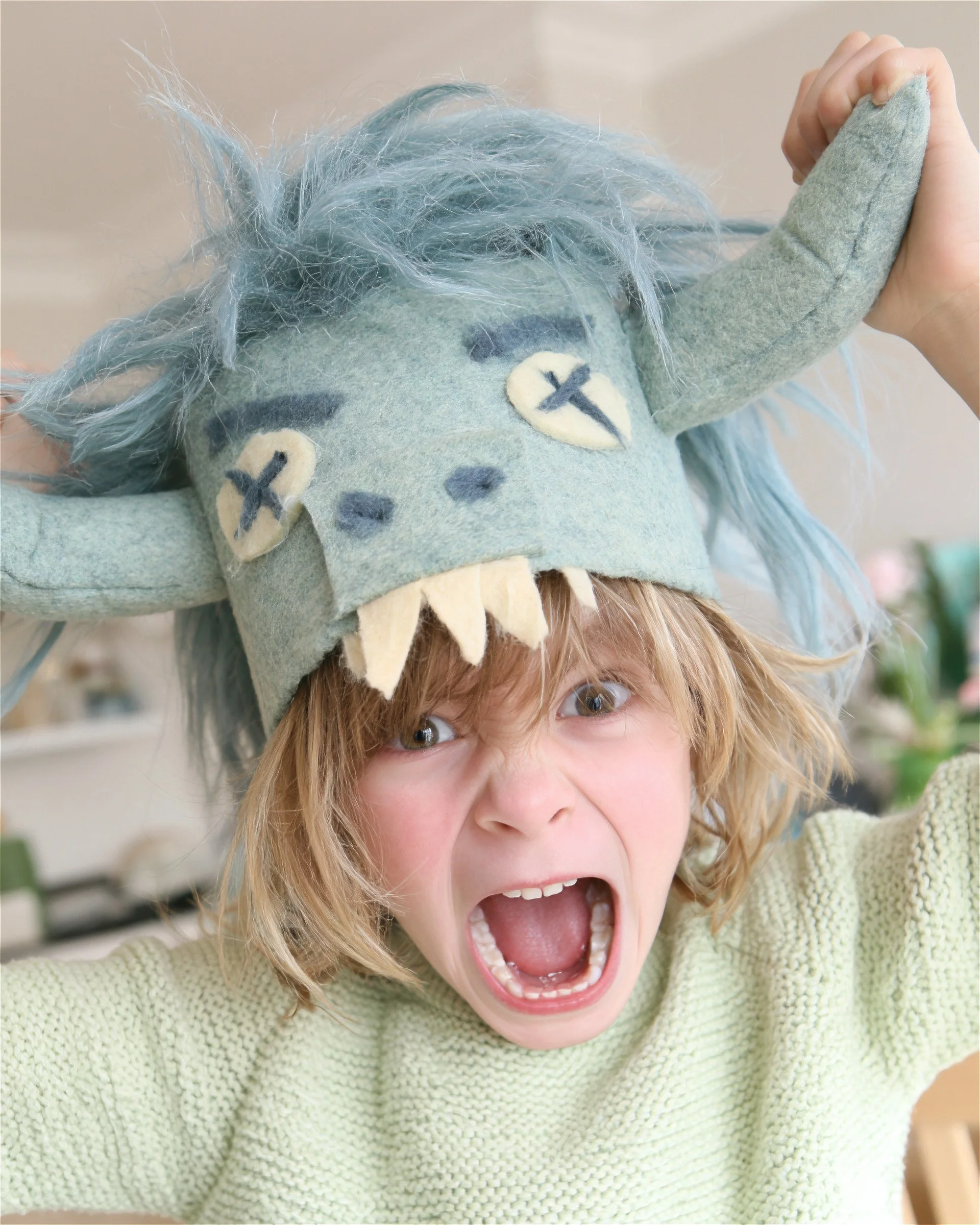 Child roaring under a blue felt monster hat. AI-generated image.