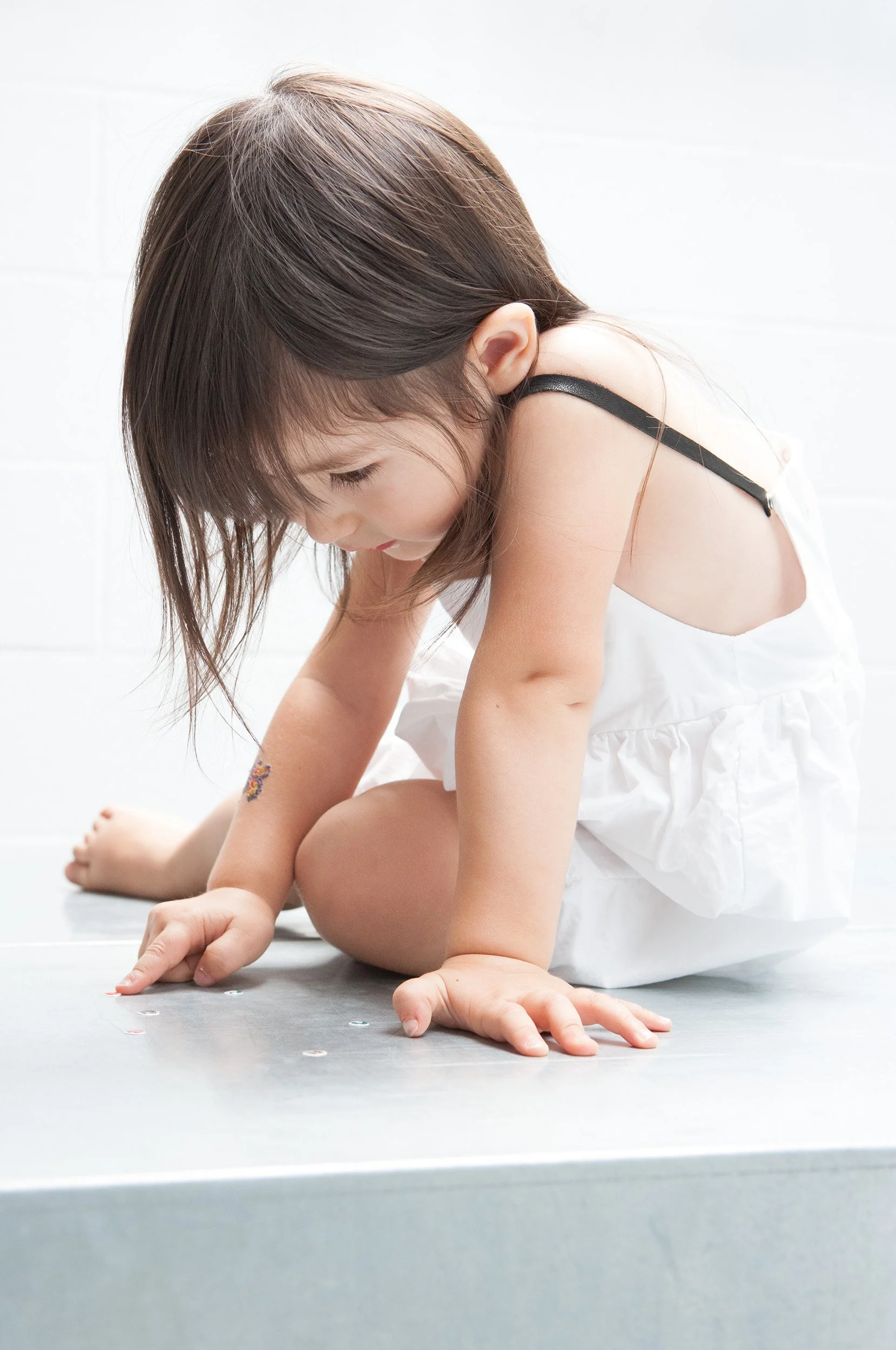 Little girl in a white cotton dress crouching on a pale floor