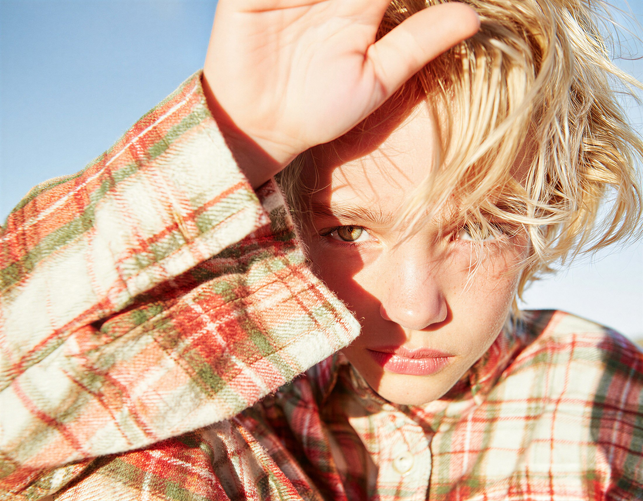 Child in a checked jacket shielding their eyes from low sunlight. AI-generated image.