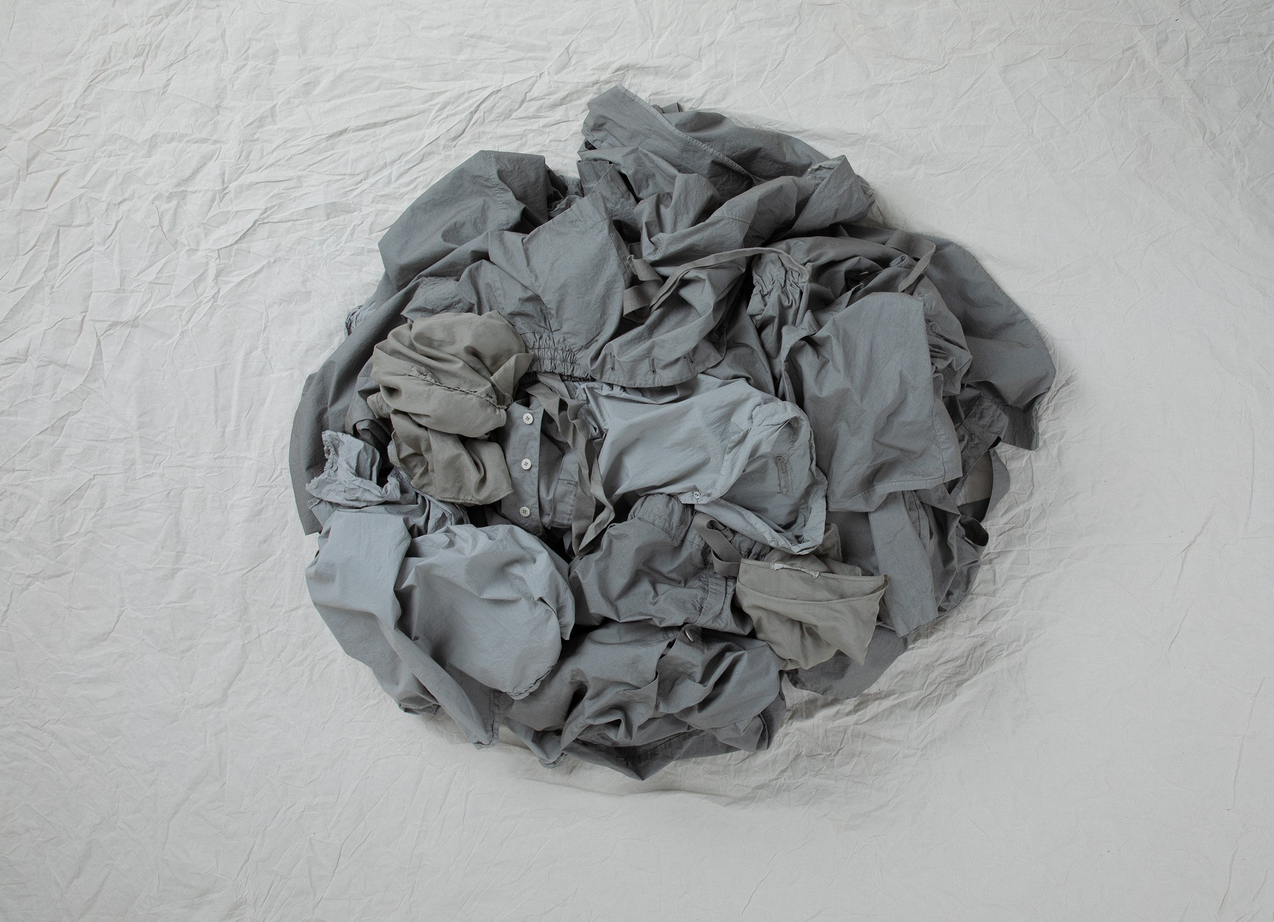 Grey clothes gathered into a circle on a crumpled white fabric, textile still file