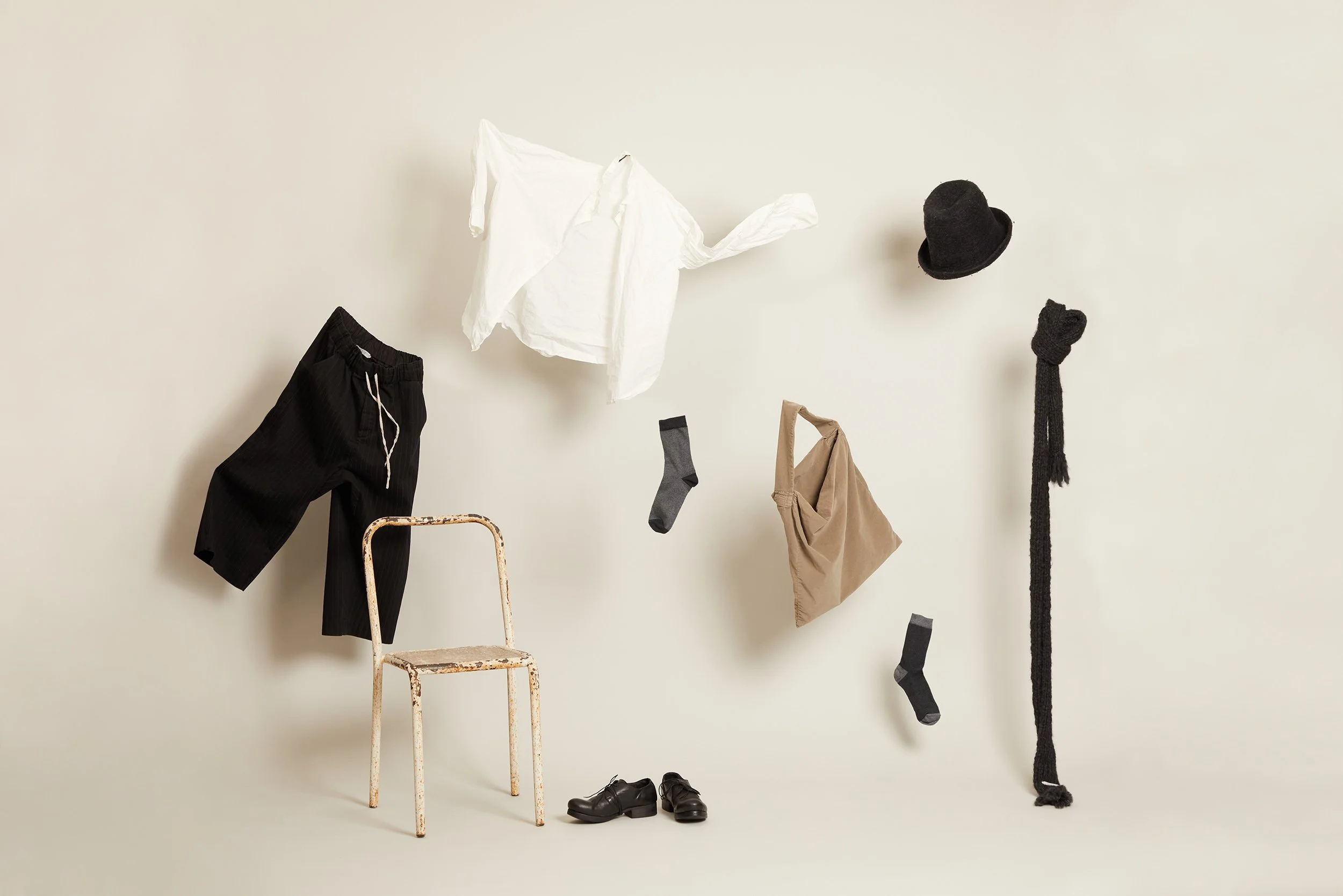 Black and white minimal clothes floating around a vintage chair on a cream wall.