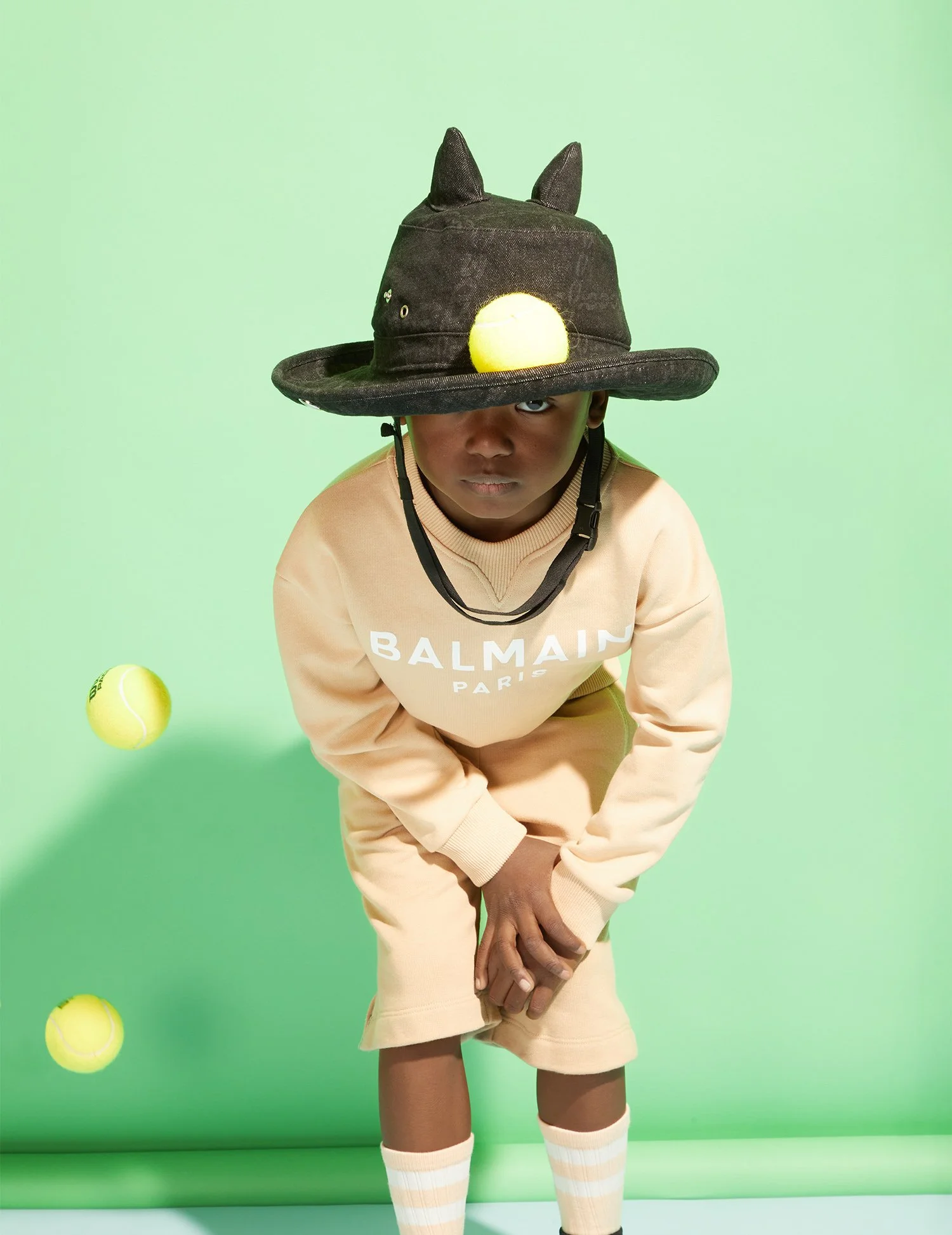 Style Piccoli editorial — hat and tennis balls on a green ground.