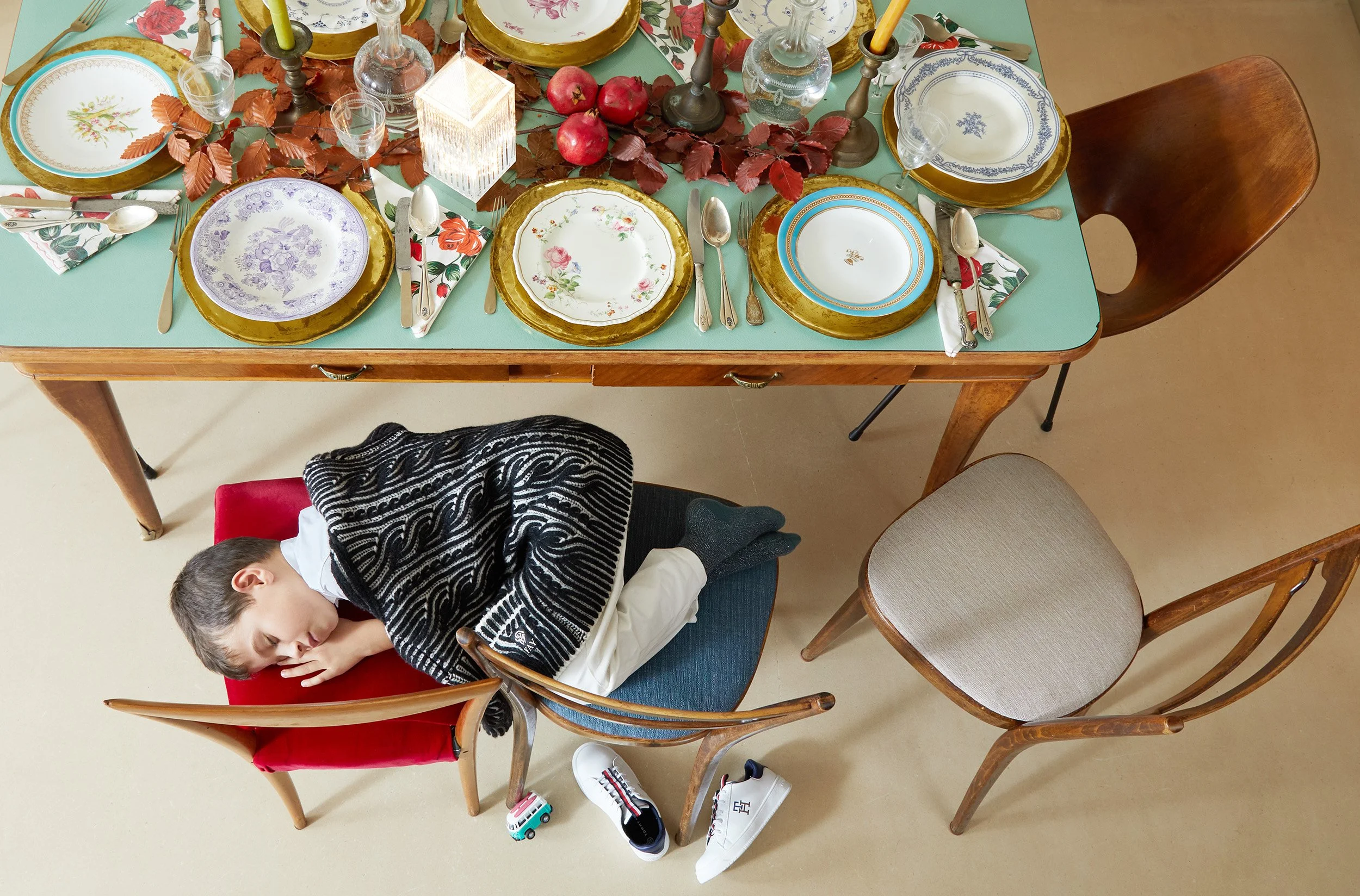 Child sleeping on chairs under a festive vintage table.