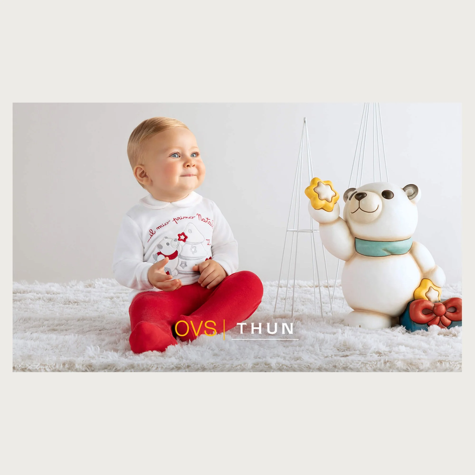 Red tights and embroidered bodysuit, baby beside a ceramic polar bear on a white rug — OVS | Thun newborn Christmas campaign.