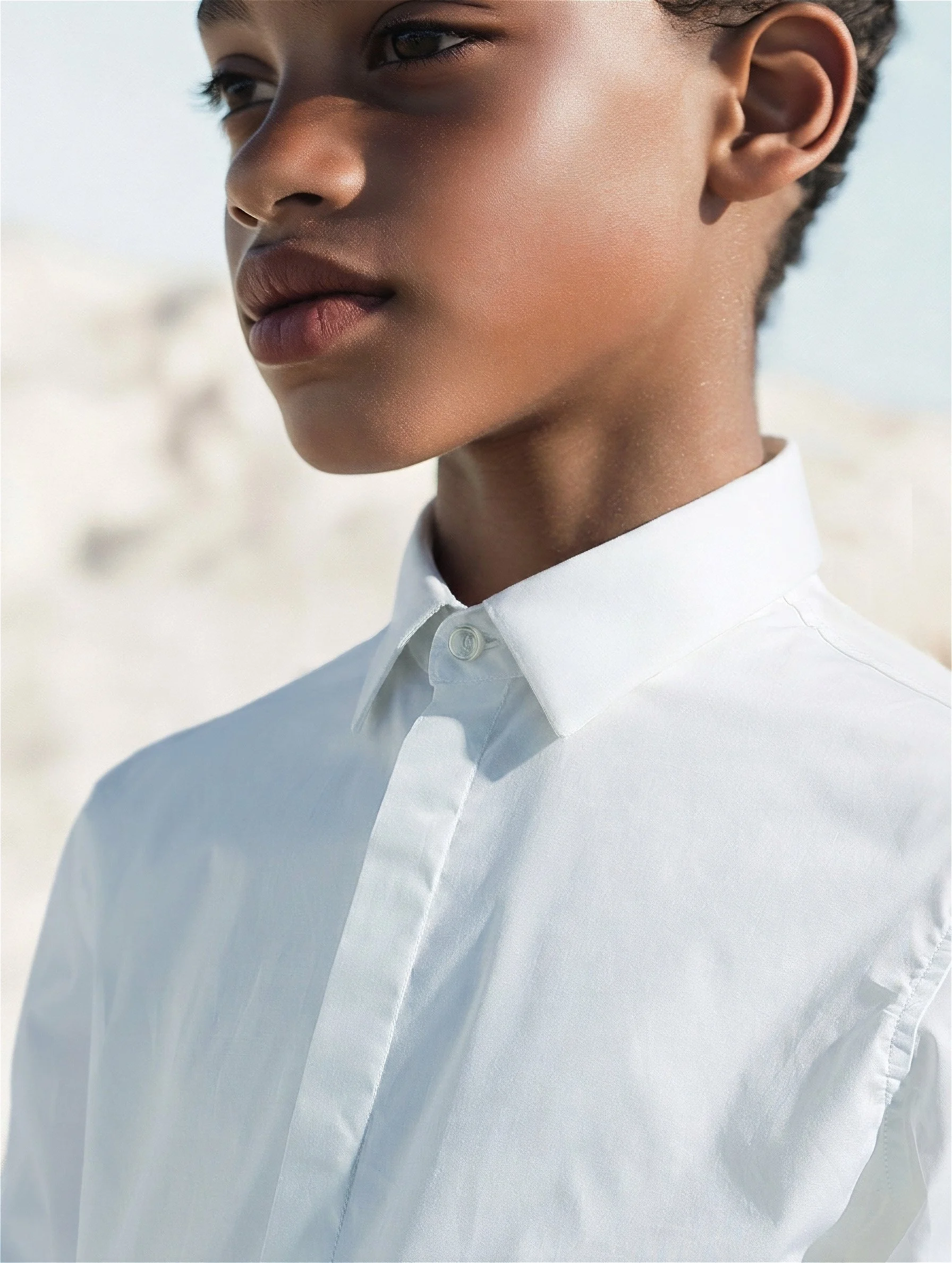 Close-up of a crisp white cotton shirt with a point collar, child turned away against pale dunes — kidswear catalogue, hard daylight. AI-generated image.