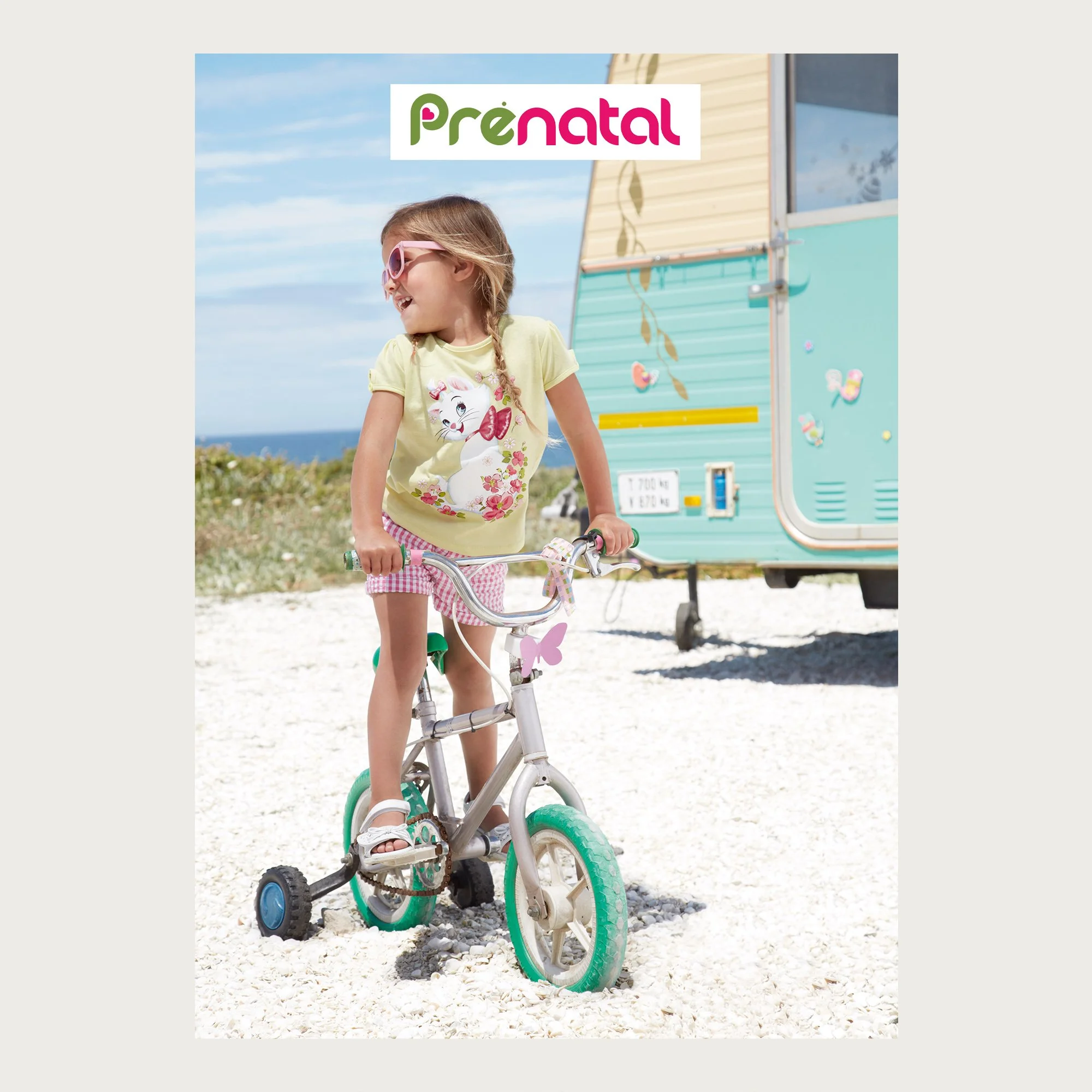 Yellow tee and gingham shorts, girl on a bike with training wheels beside a mint caravan, cape town, Prénatal campaign.