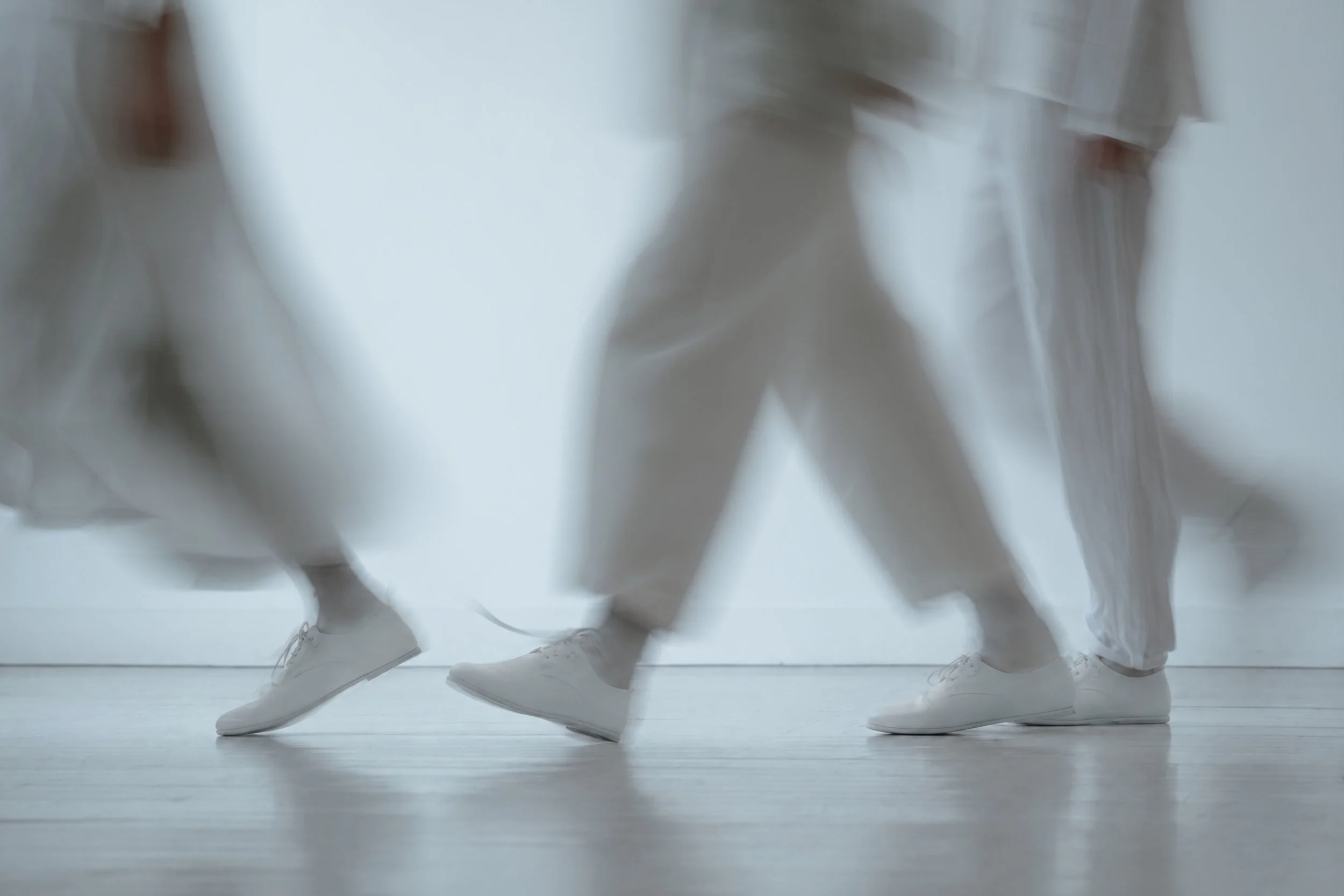 Legs in white trousers and leather shoes walking across a studio floor, motion blur. AI-generated image.