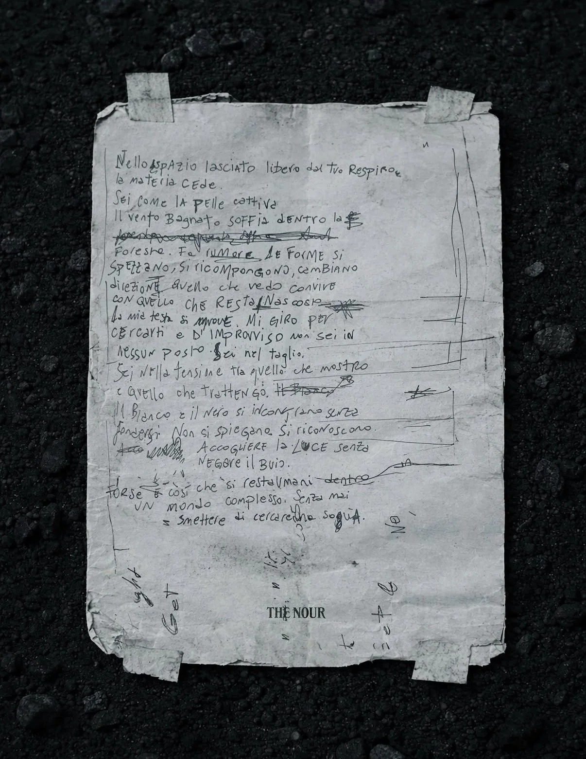 A crumpled and torn handwritten note in Italian, taped to the ground with black soil surrounding it.