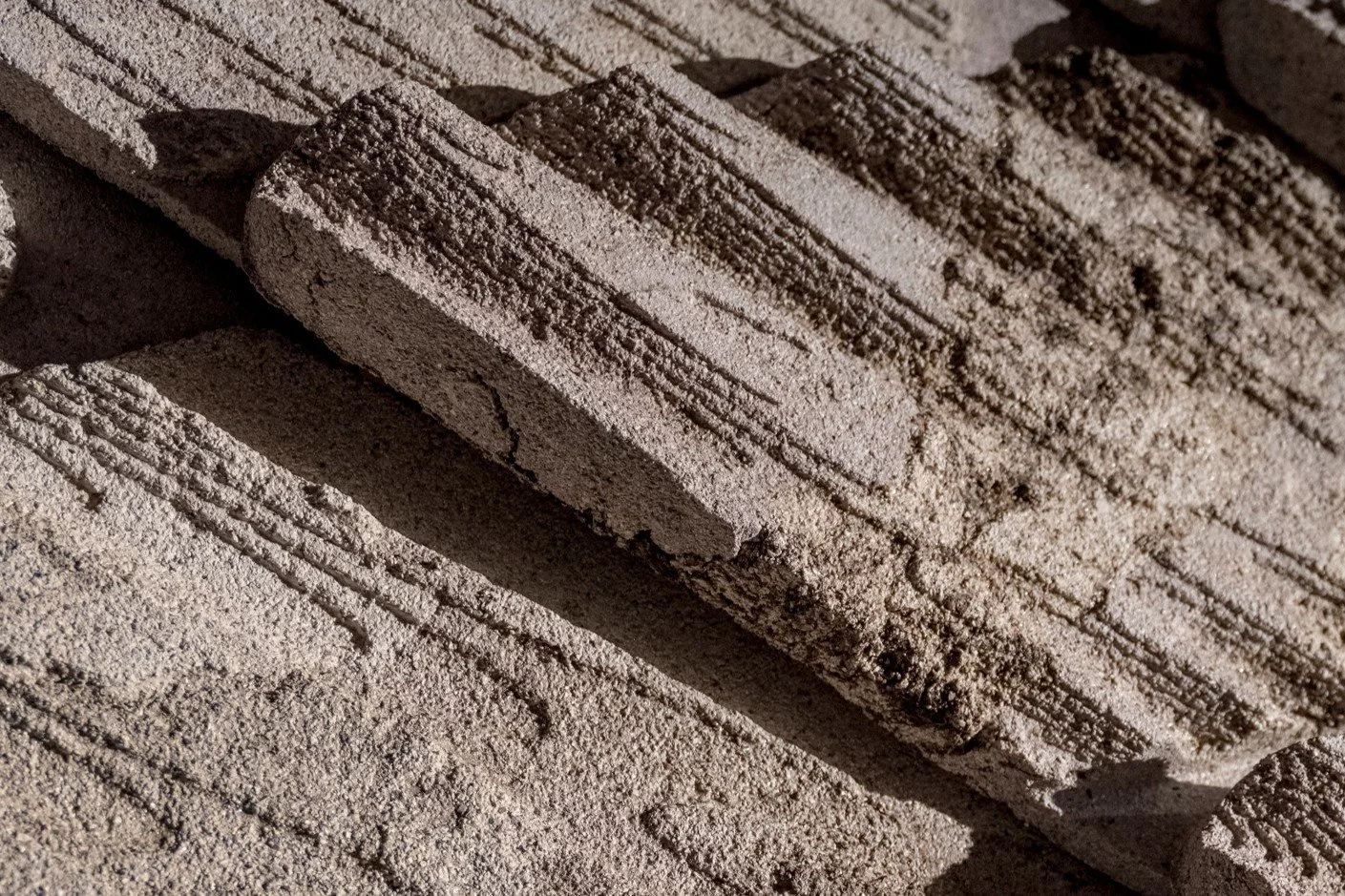 Close-up of a stack of bricks with textured surfaces and visible grooves, with some bricks casting shadows.
