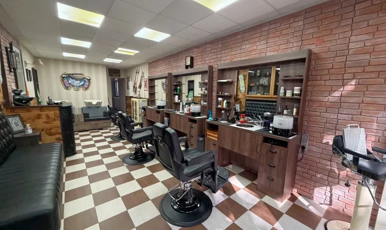 Salon de coiffure avec plusieurs fauteuils, miroirs, et stations de coiffure contre un mur en briques, avec un sol en carreaux beige et marron.