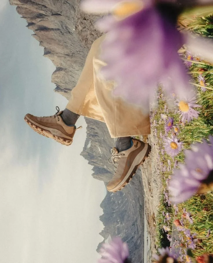 Une aventurière outdoor couchée dans un champ de fleurs avec des montagnes en arrière-plan.
