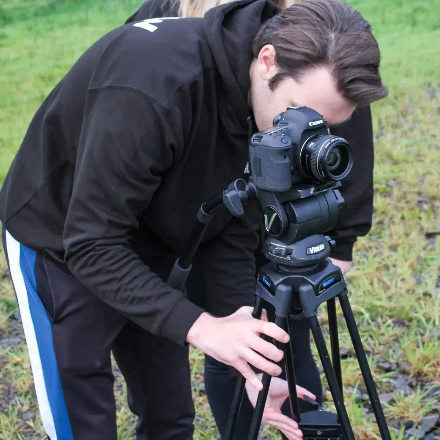 A person operating a professional video camera outdoors in a grassy area.