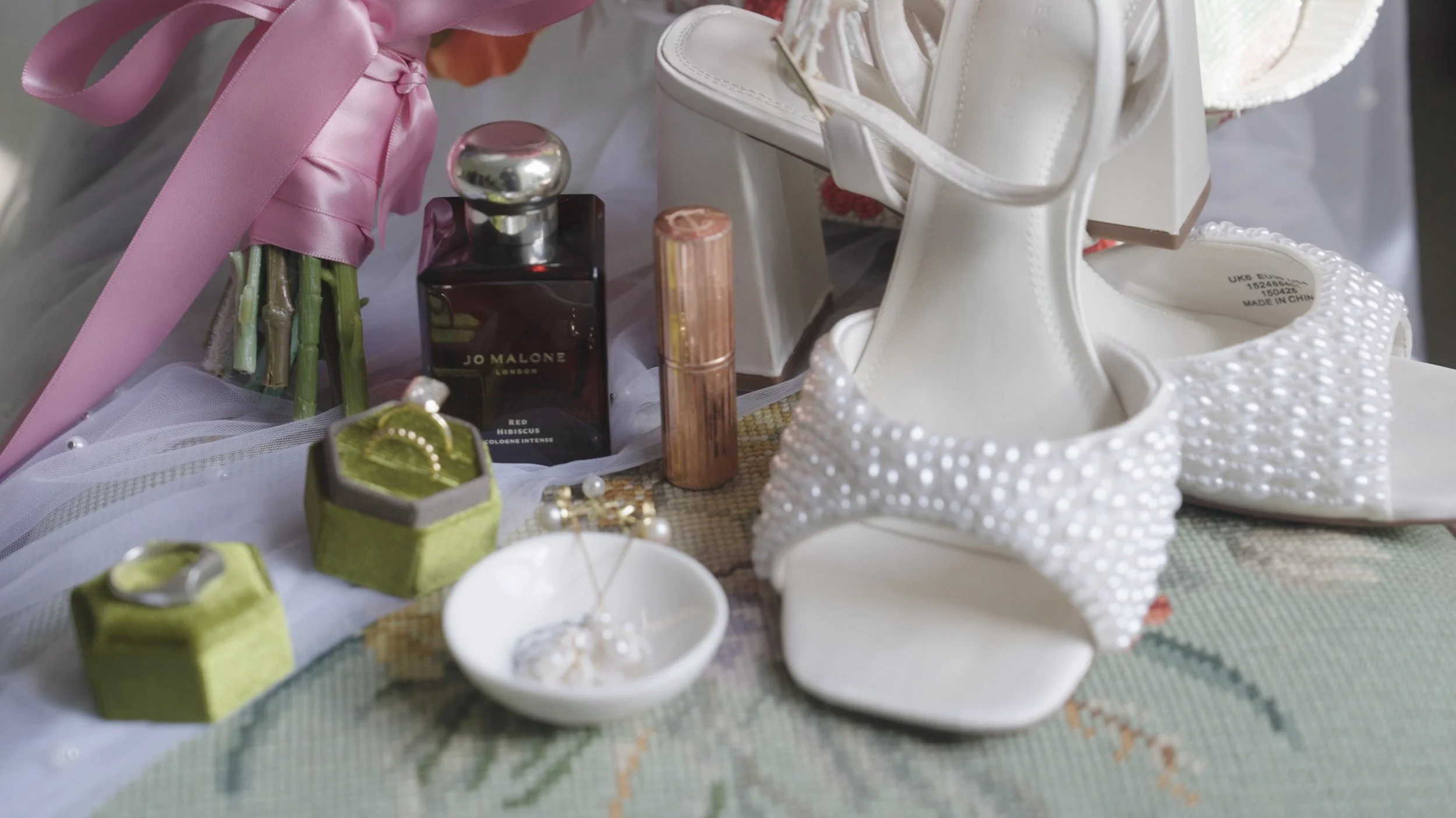 Wedding shoes, perfume, jewelry, and small decorative boxes with rings on a table.