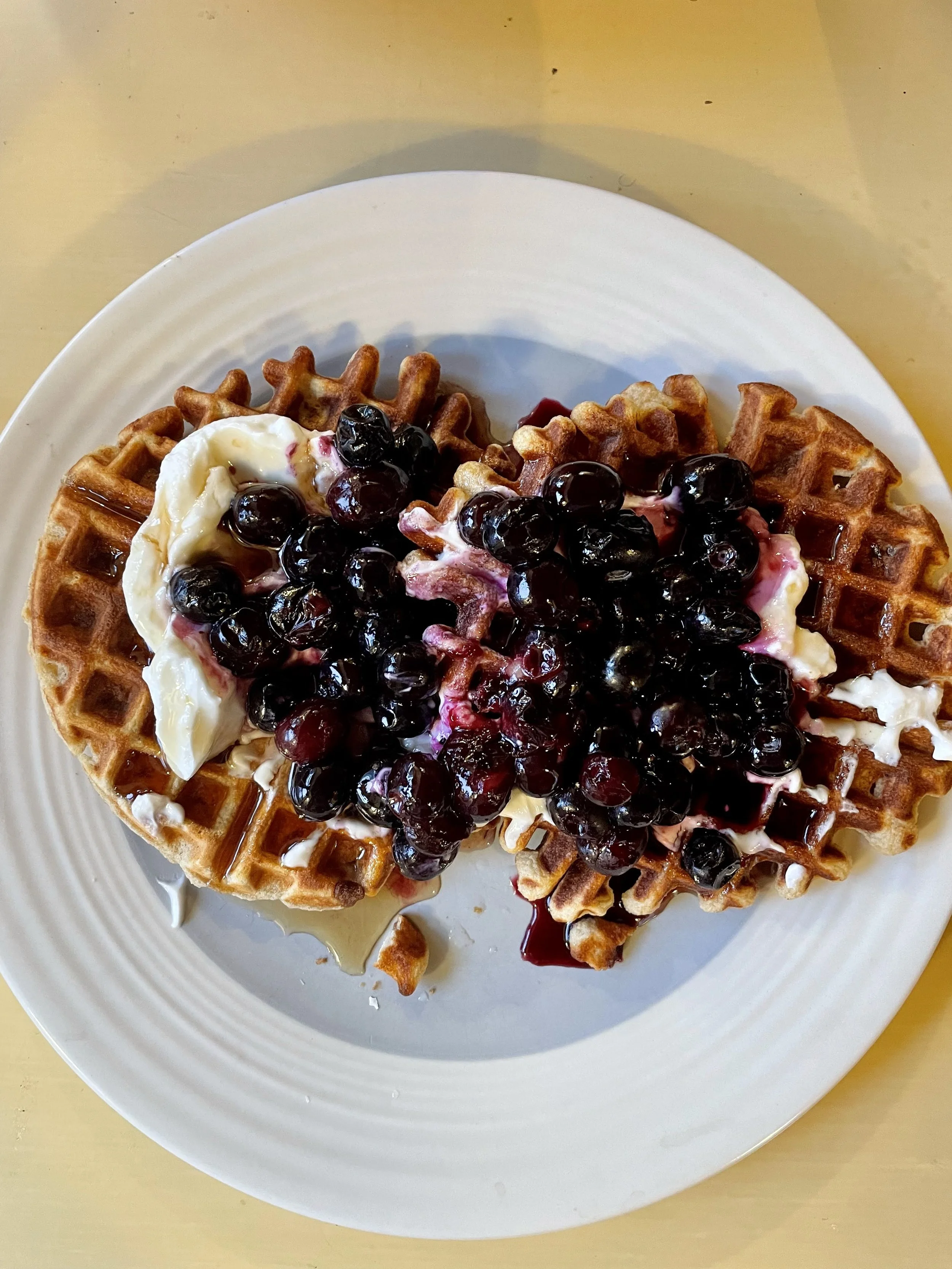 Waffles topped with blueberries, banana slices, and syrup on a white plate.