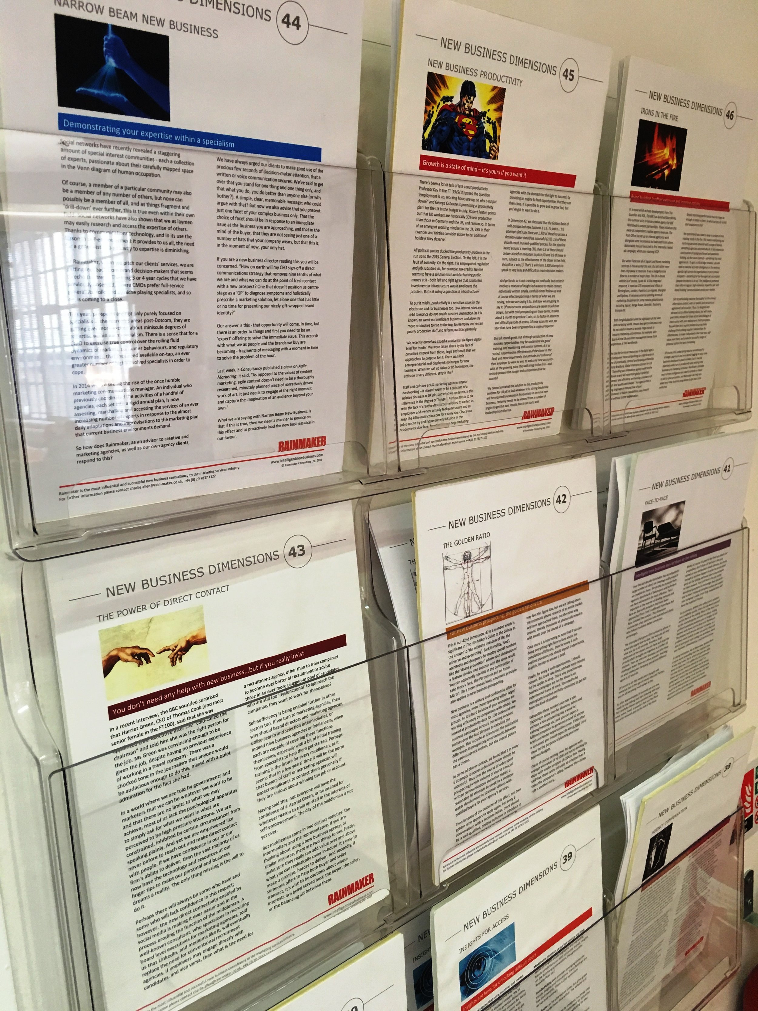 Display of multiple brochures and magazines about new business dimensions in a wire rack, with visible titles and text on the pages.