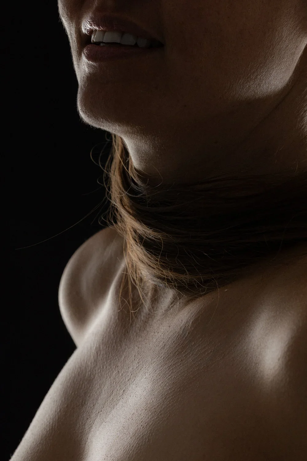 Close-up of a woman's face and neck in soft lighting against a dark background.