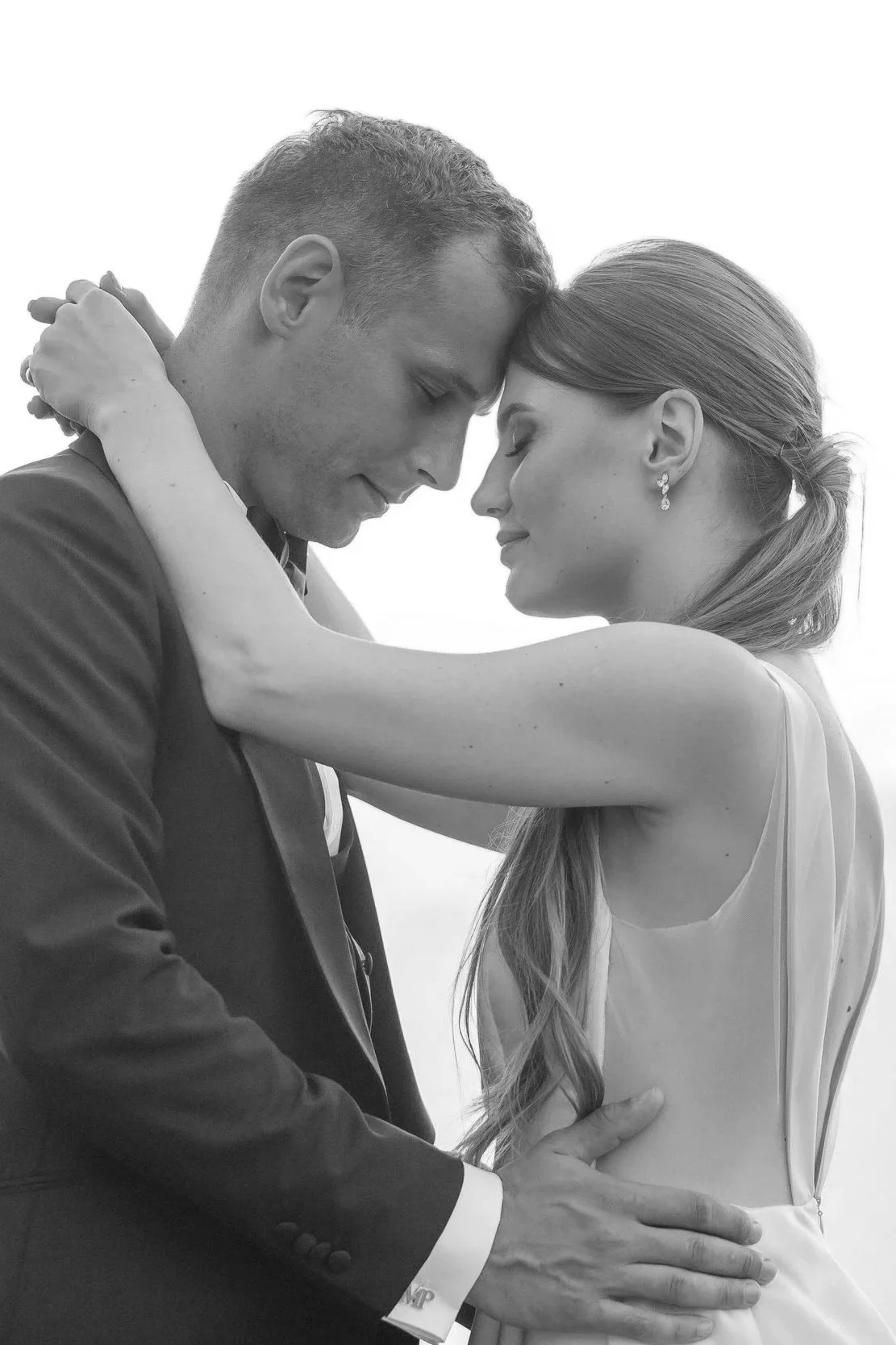 Black and white photo of a man and woman in an affectionate embrace, with foreheads touching and eyes closed, standing close with arms around each other.