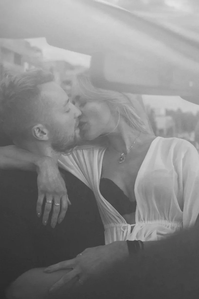 A black and white photo of a man and woman sharing a kiss, with their eyes closed. The woman has her hand on the man's shoulder.