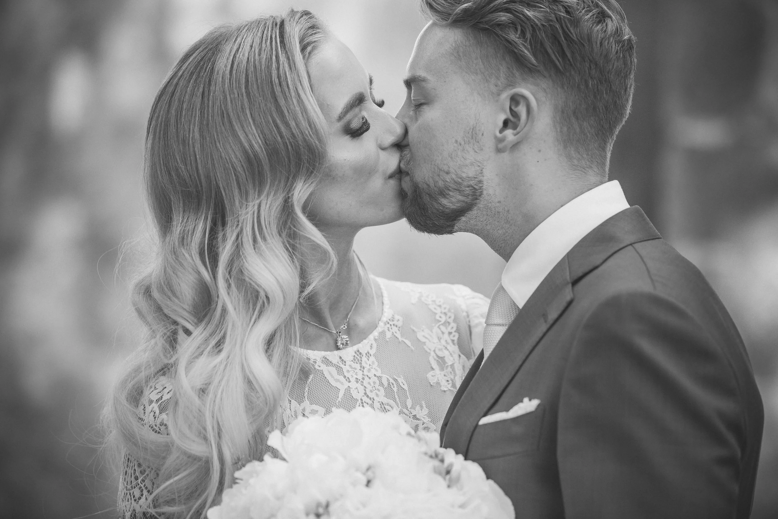 Black and white photo of a bride and groom sharing a kiss during their wedding, with the bride holding a bouquet.