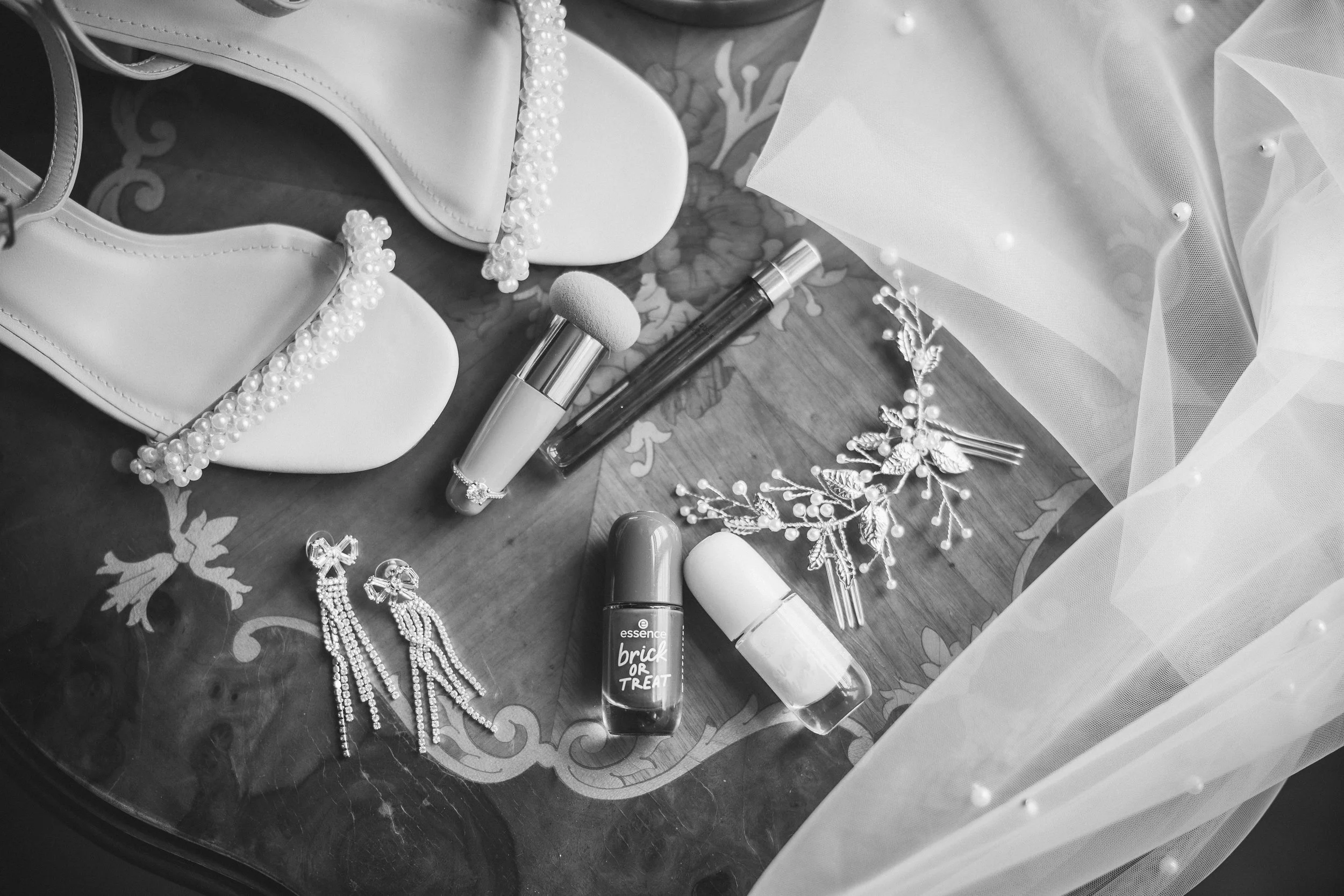 A flat surface with various jewelry pieces, cosmetics, and decorative items. Visible are a pearl necklace, dangling earrings, two lipsticks, a spray bottle, a container, and decorative hair accessories. The surface is covered with a tablecloth, and s