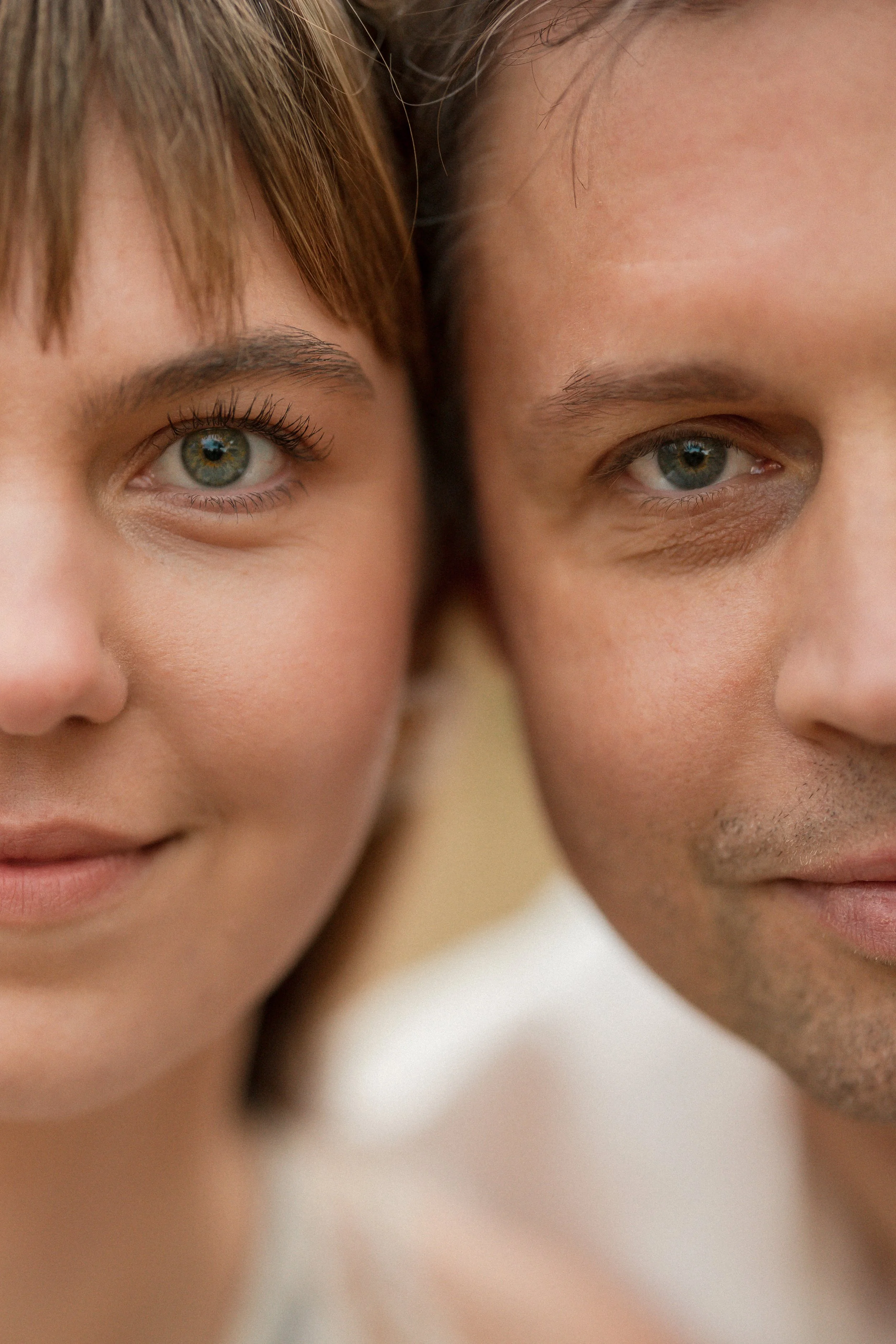 Close-up of two smiling individuals, one woman and one man, showing half of their faces with a focus on their eyes and lips, against a neutral background.