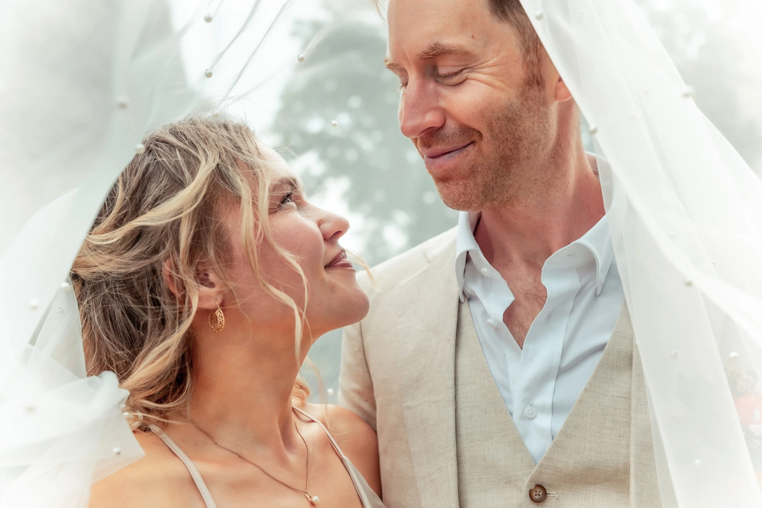 A bride and groom smiling and looking at each other under a wedding veil.
